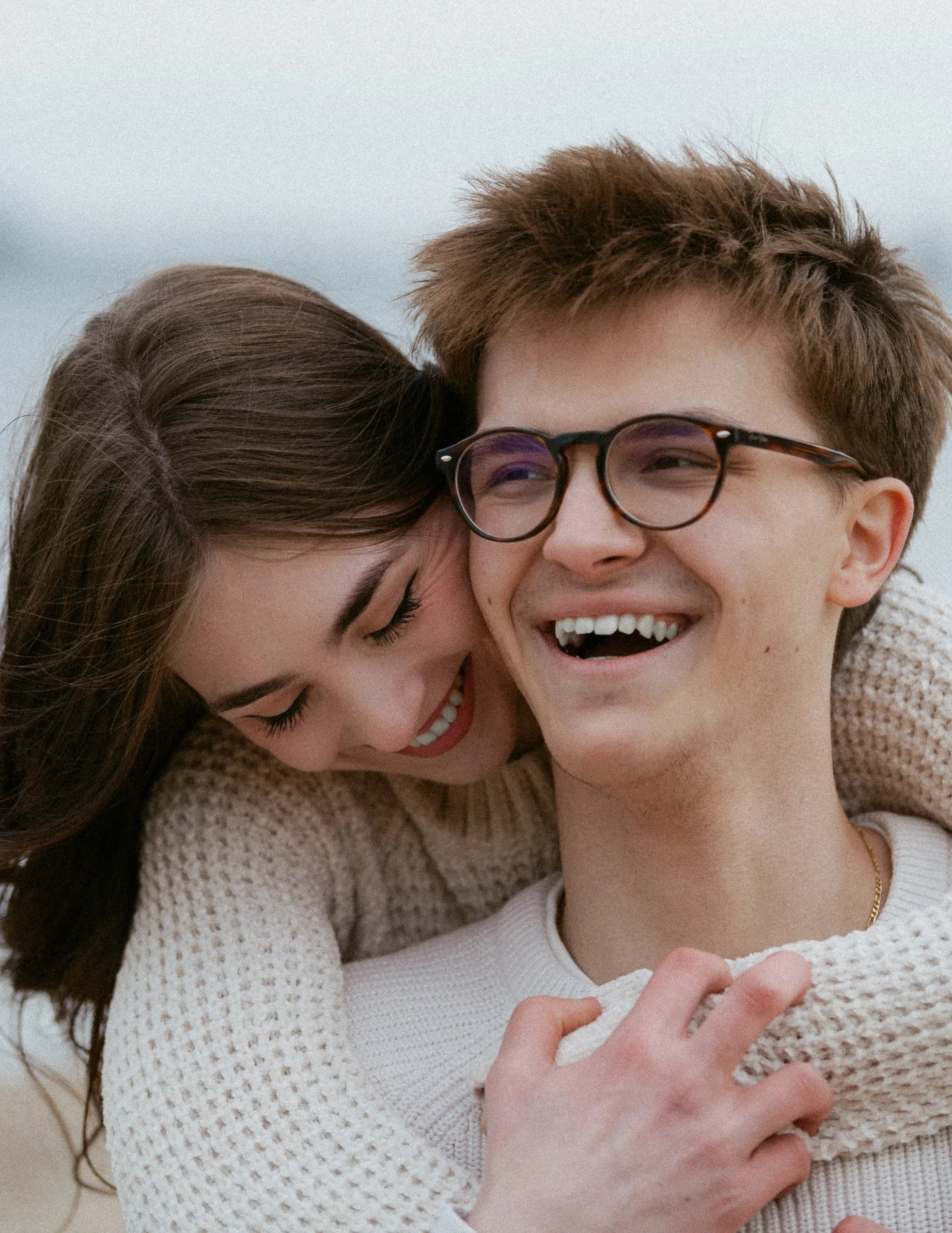 A young couple is happily embracing and smiling at each other outdoors.