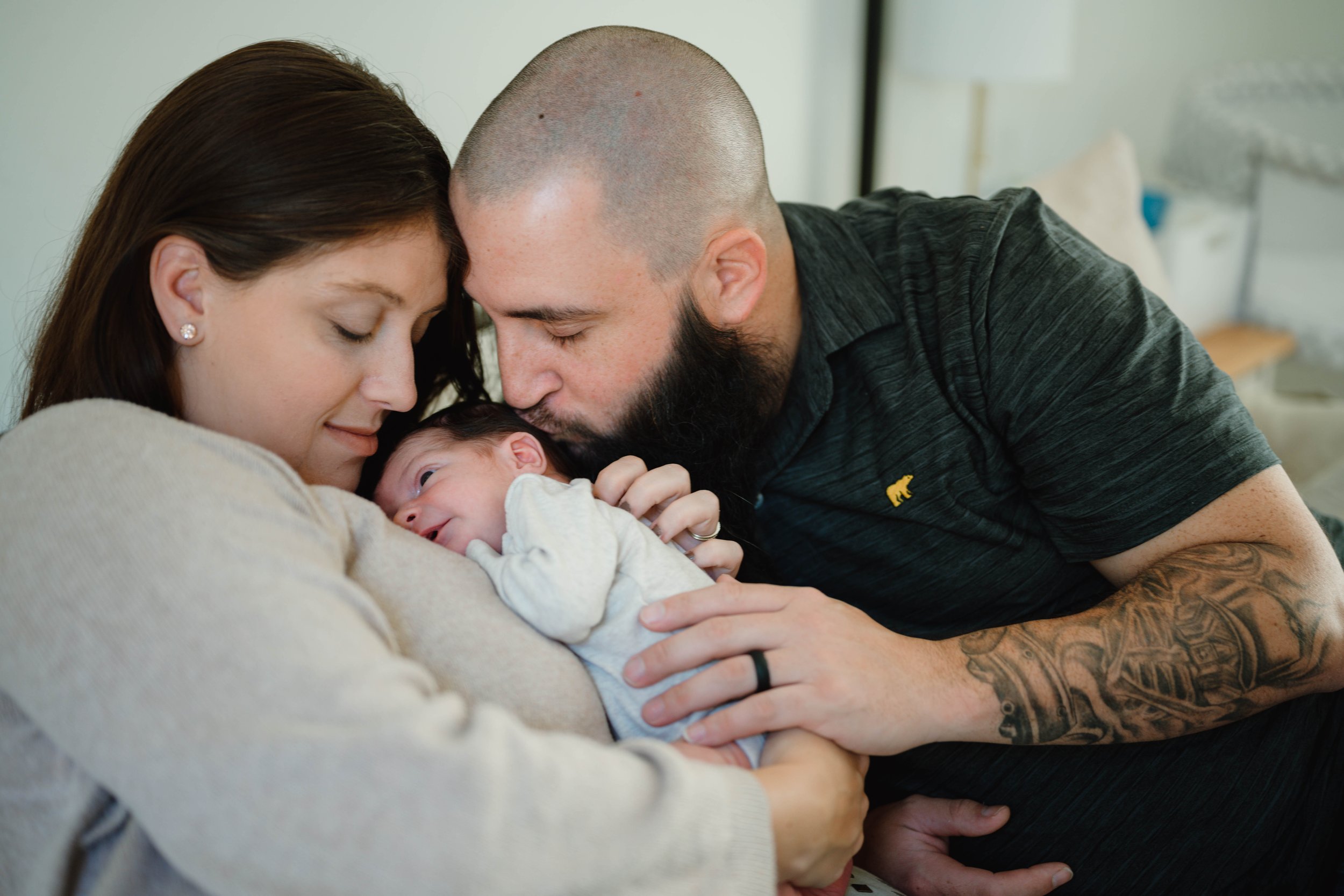 Dad kisses newborn baby as mom snuggles him close