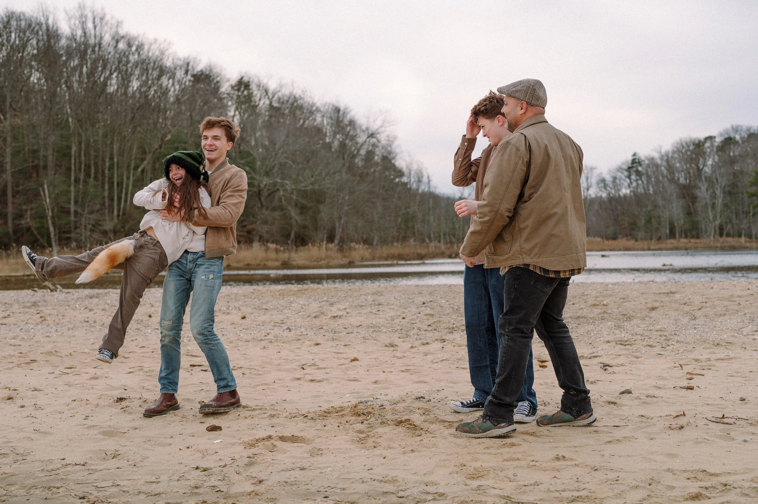 Older brother twirls little sister while father and brother look on beach