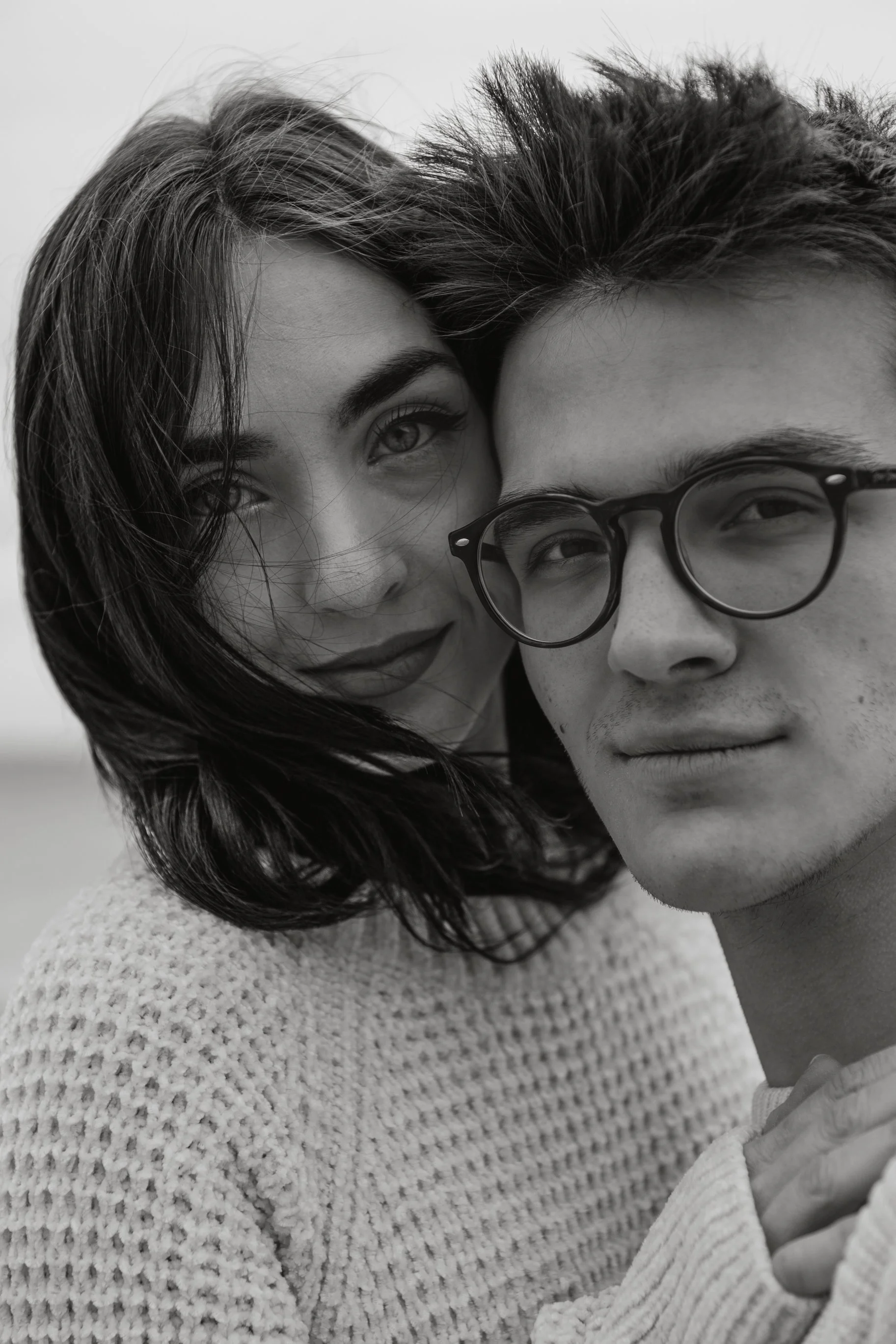 Close-up of a man and woman taking a selfie together outdoors, both facing the camera, with the woman smiling and the man wearing glasses.
