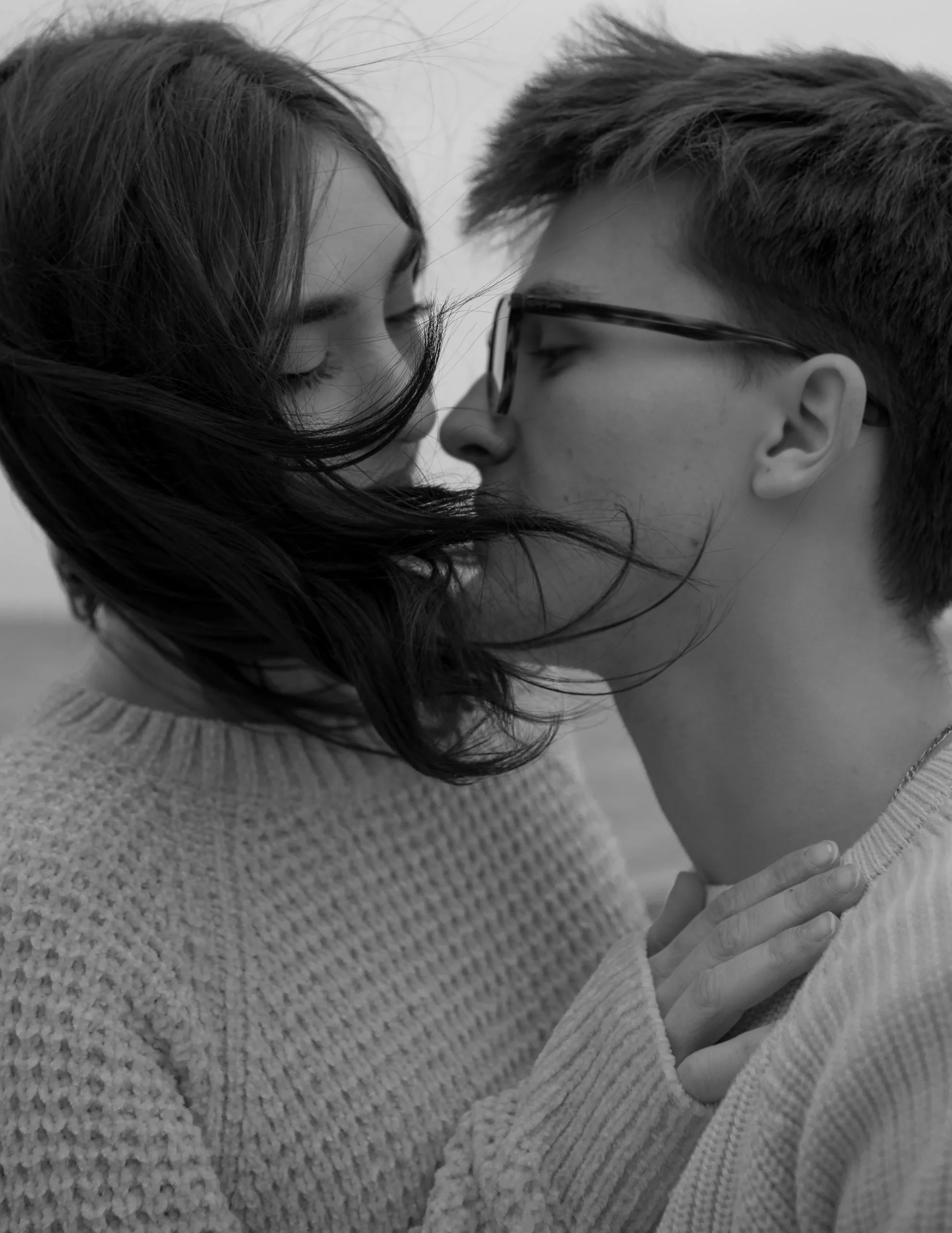 A black-and-white photo of a young woman and man close face-to-face, with eyes closed, about to kiss outdoors.
