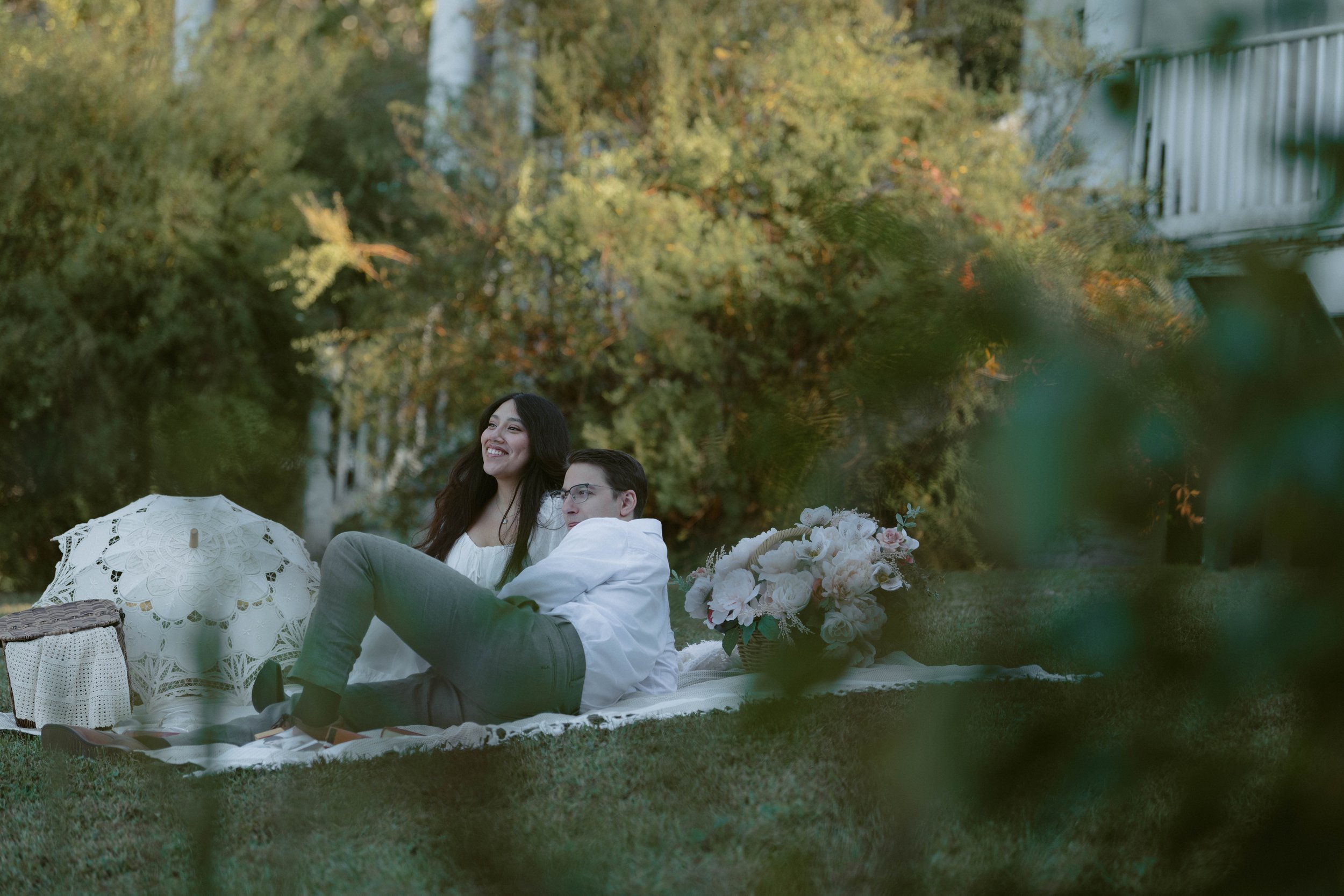 Couple relaxing on a blanket during a film-inspired engagement session at Chapman State Park in Indian Head, Maryland, surrounded by greenery, picnic details, and soft autumn light.