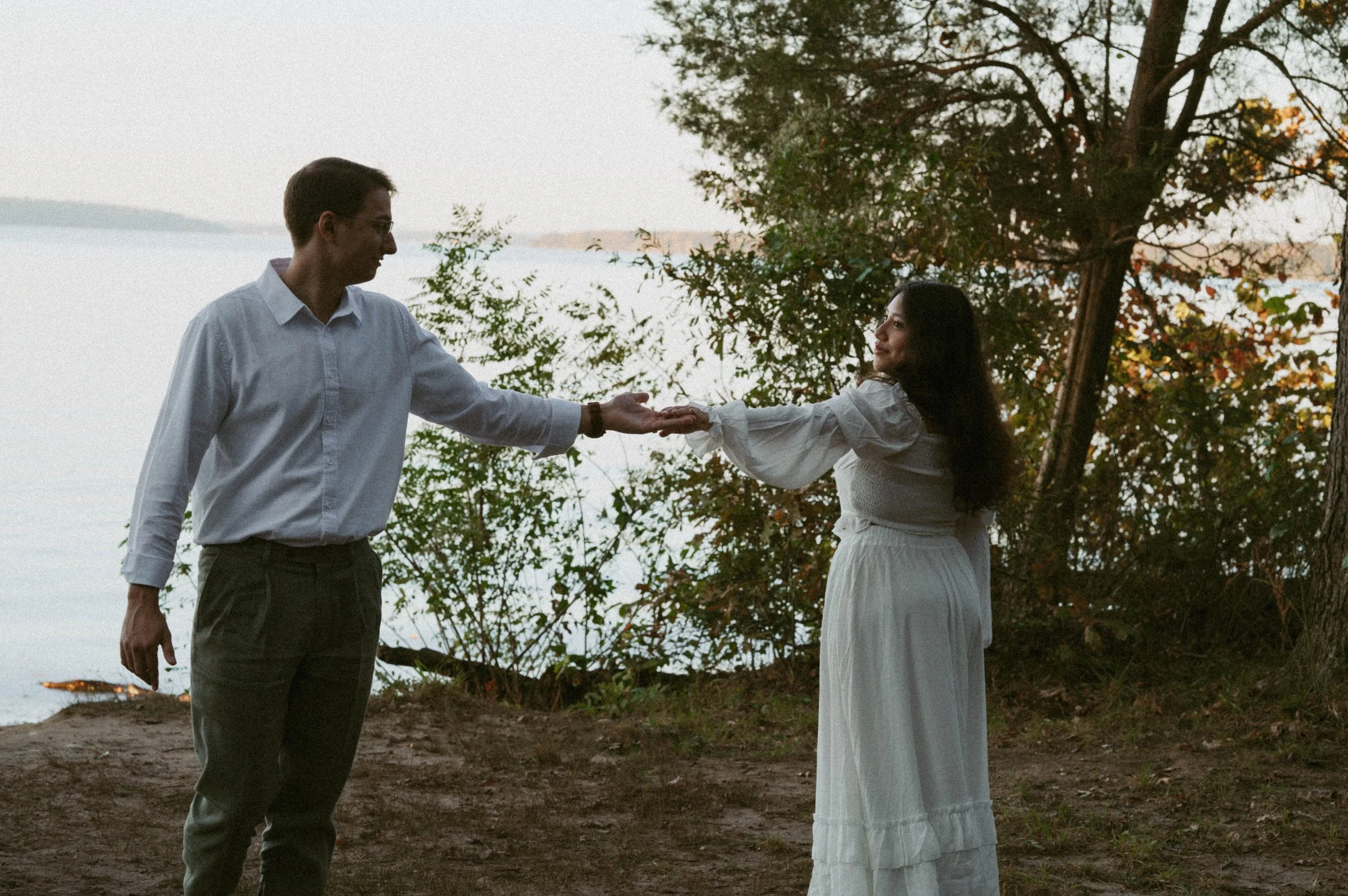 Engaged couple holding hands along the waterfront during a film-inspired engagement session at Chapman State Park in Indian Head, Maryland, photographed in the DC, Maryland, and Virginia (DMV) area.
