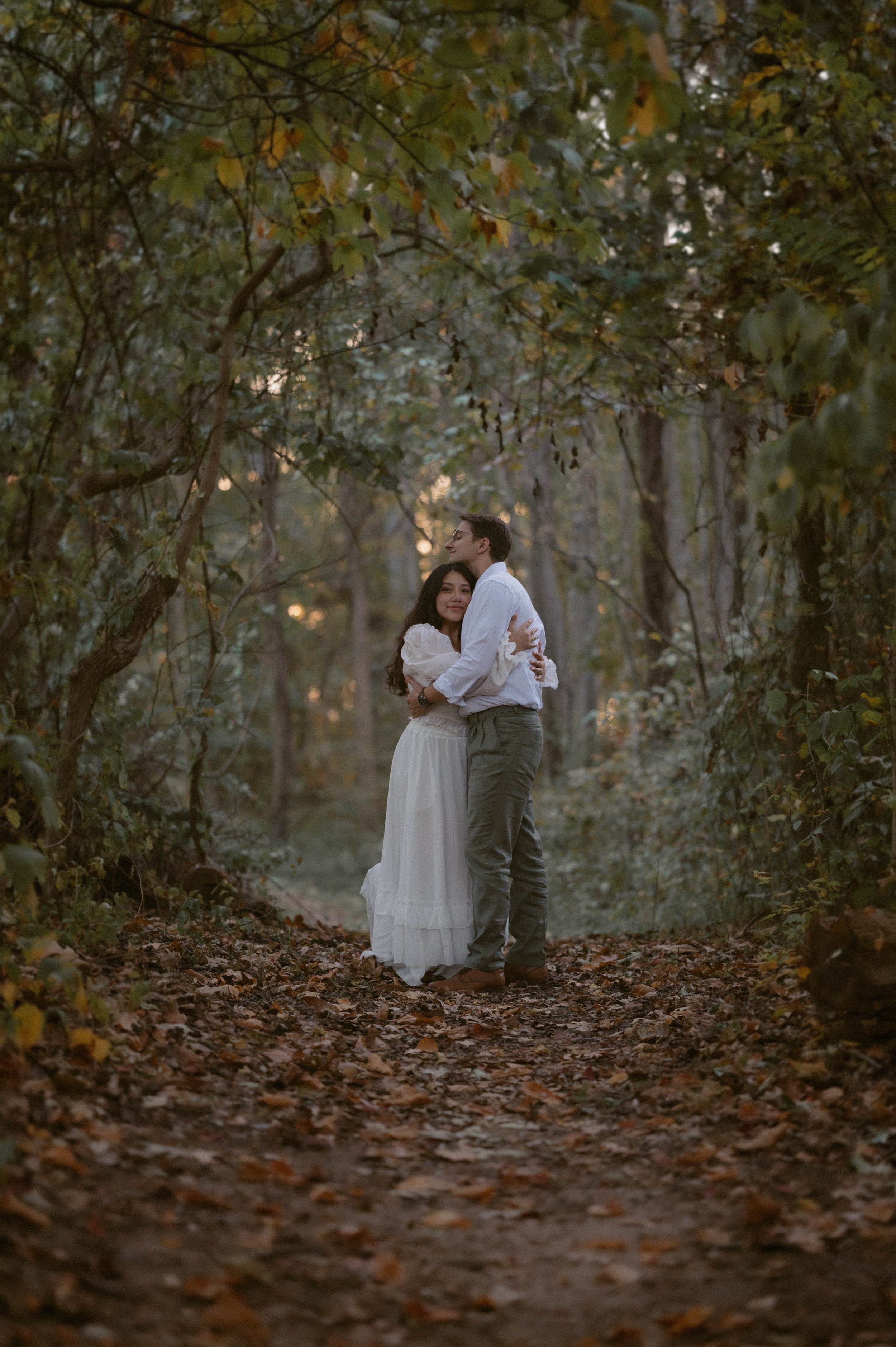 Engaged couple embraces along a wooded trail during a green, film-inspired engagement session - Olea & Co Photography - Southern Maryland Engagement Session