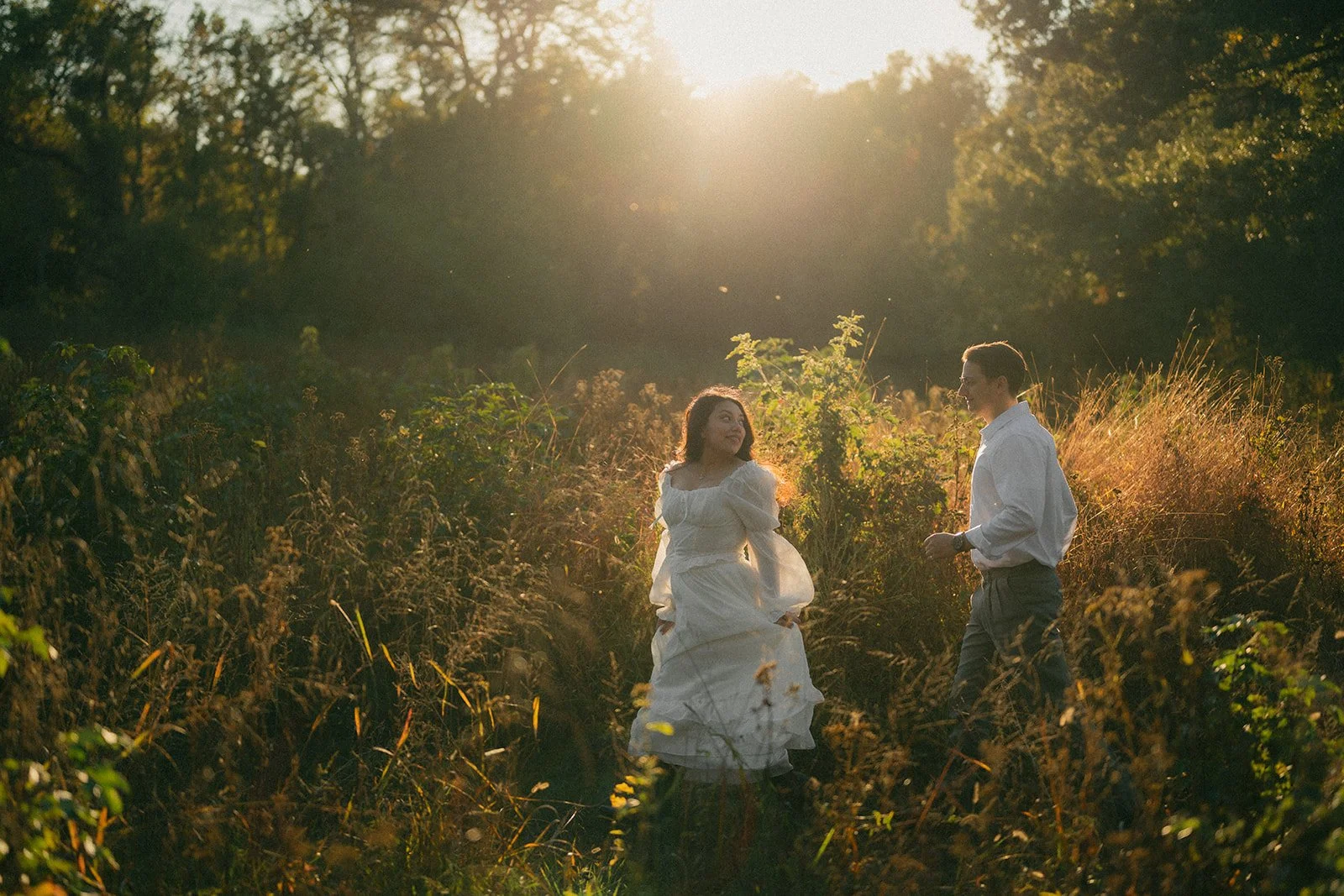 ouple walking through sunlit field during Pride and Prejudice–inspired engagement photoshoot in Southern Maryland.