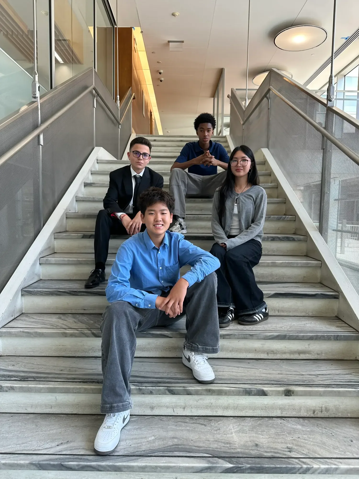 Group of five teenagers sitting on marble staircase inside modern building.
