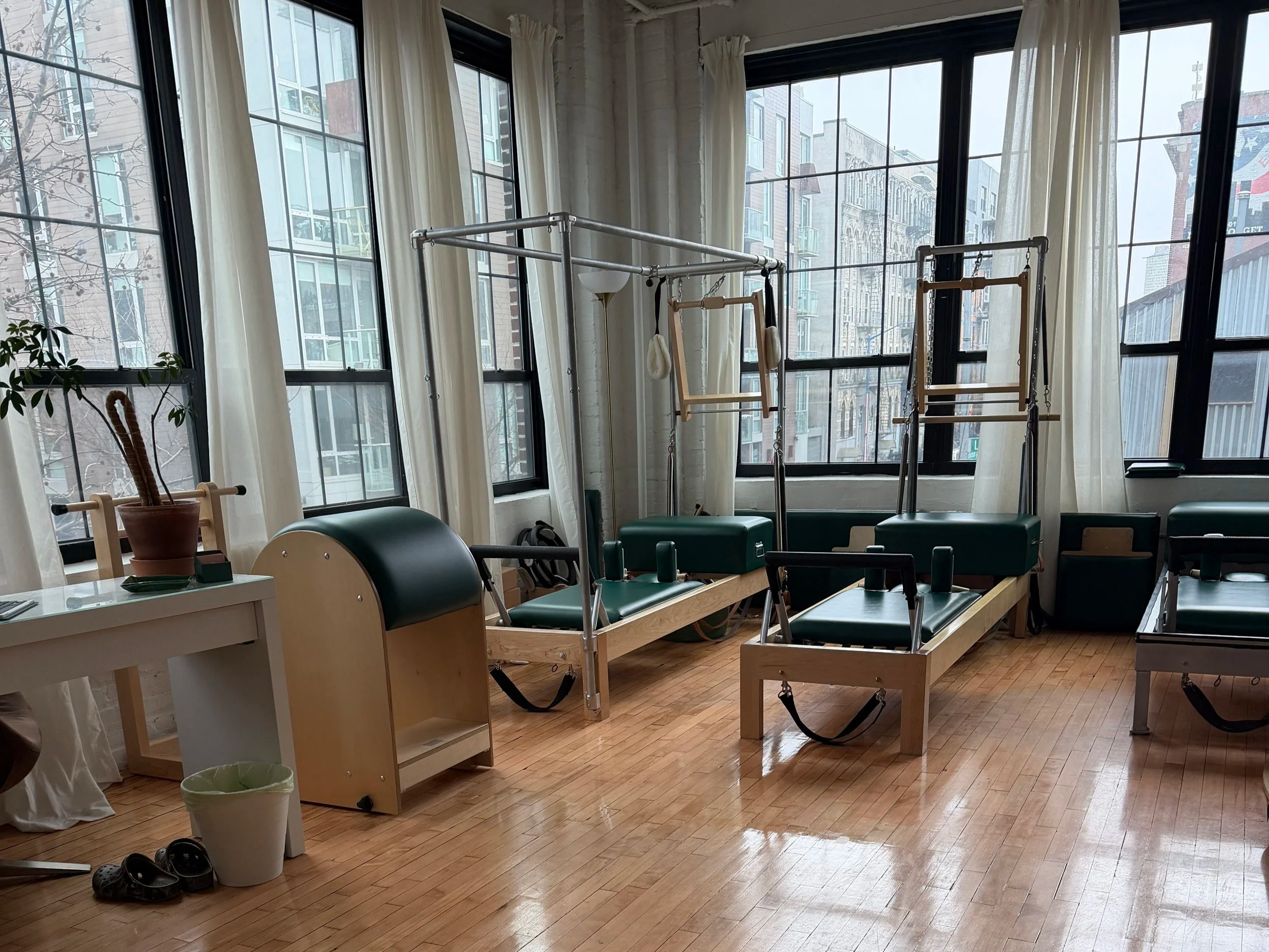 Interior of a room with large windows, wooden floor, and yoga or exercise equipment including a wooden wall-mounted bar, gymnastics rings, and a padded bench.