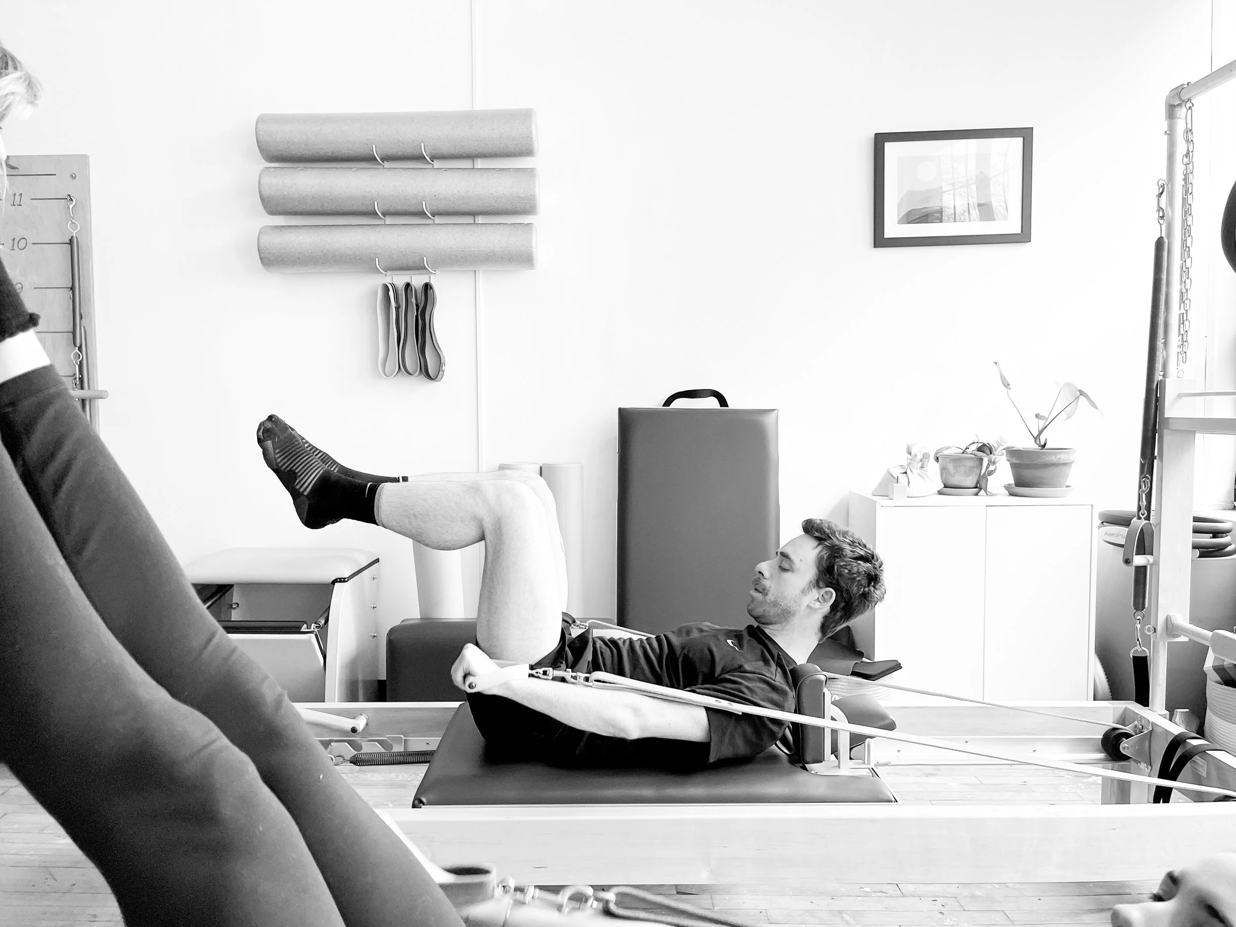 strong man on pilates reformer with knees lifted and arms stretched in straps