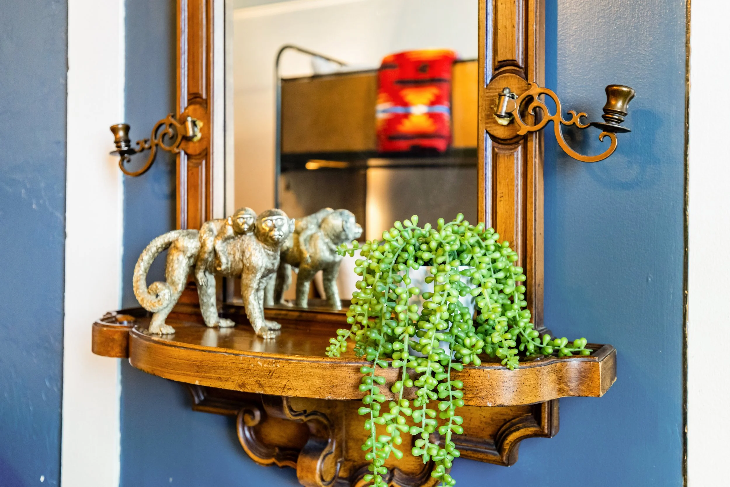 Image of decor in Room 1, a thrifted mirror with a monkey and baby monkey statue and a potted plant on the shelf. The bunk beds are visible in the mirror.