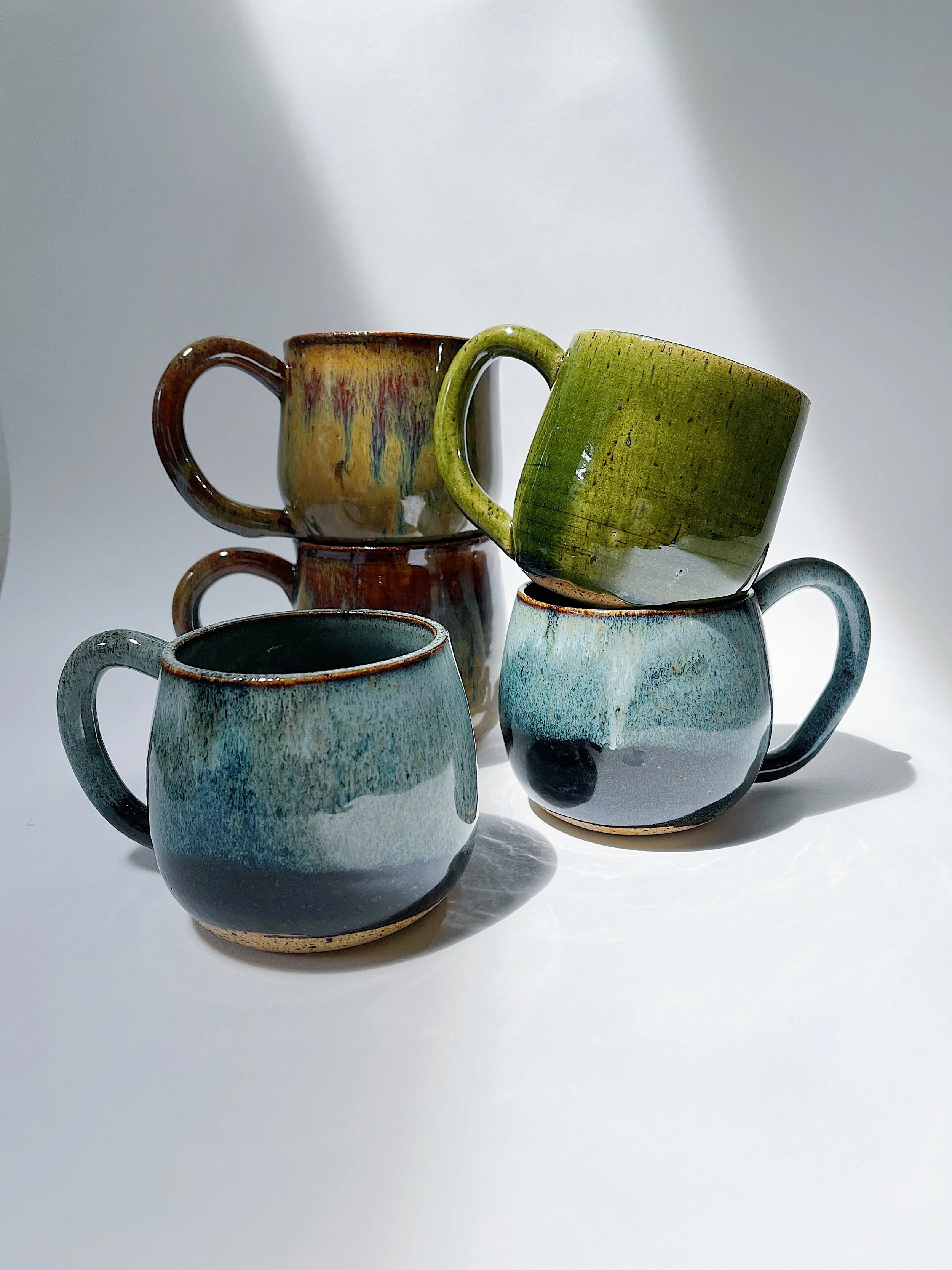 Colorful ceramic mugs stacked and arranged on a white surface with light shining and casting shadows.