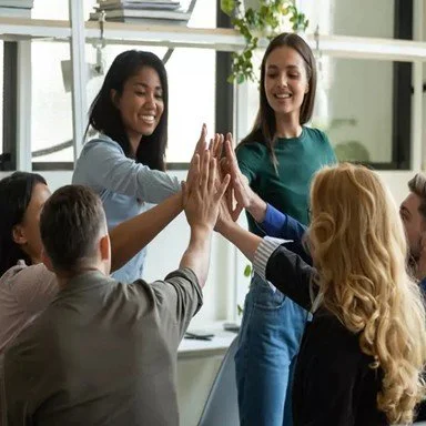 Group of diverse young adults giving each other high fives indoors.