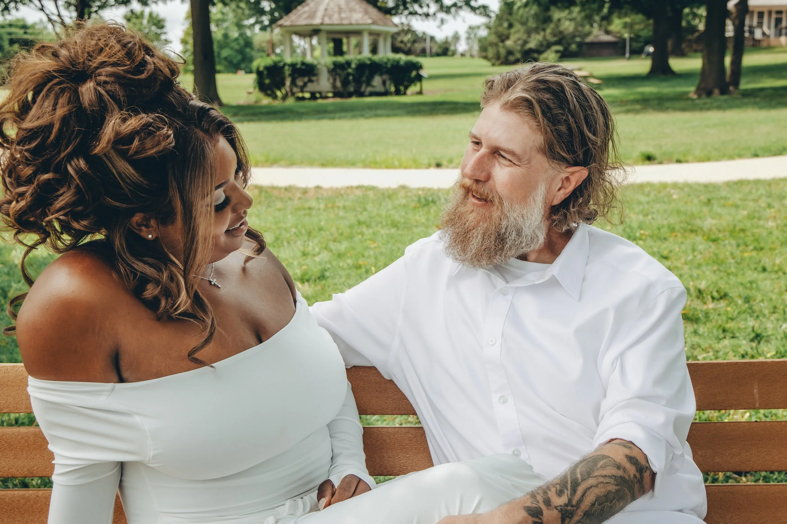 bride listens to groom while smiling on a bench