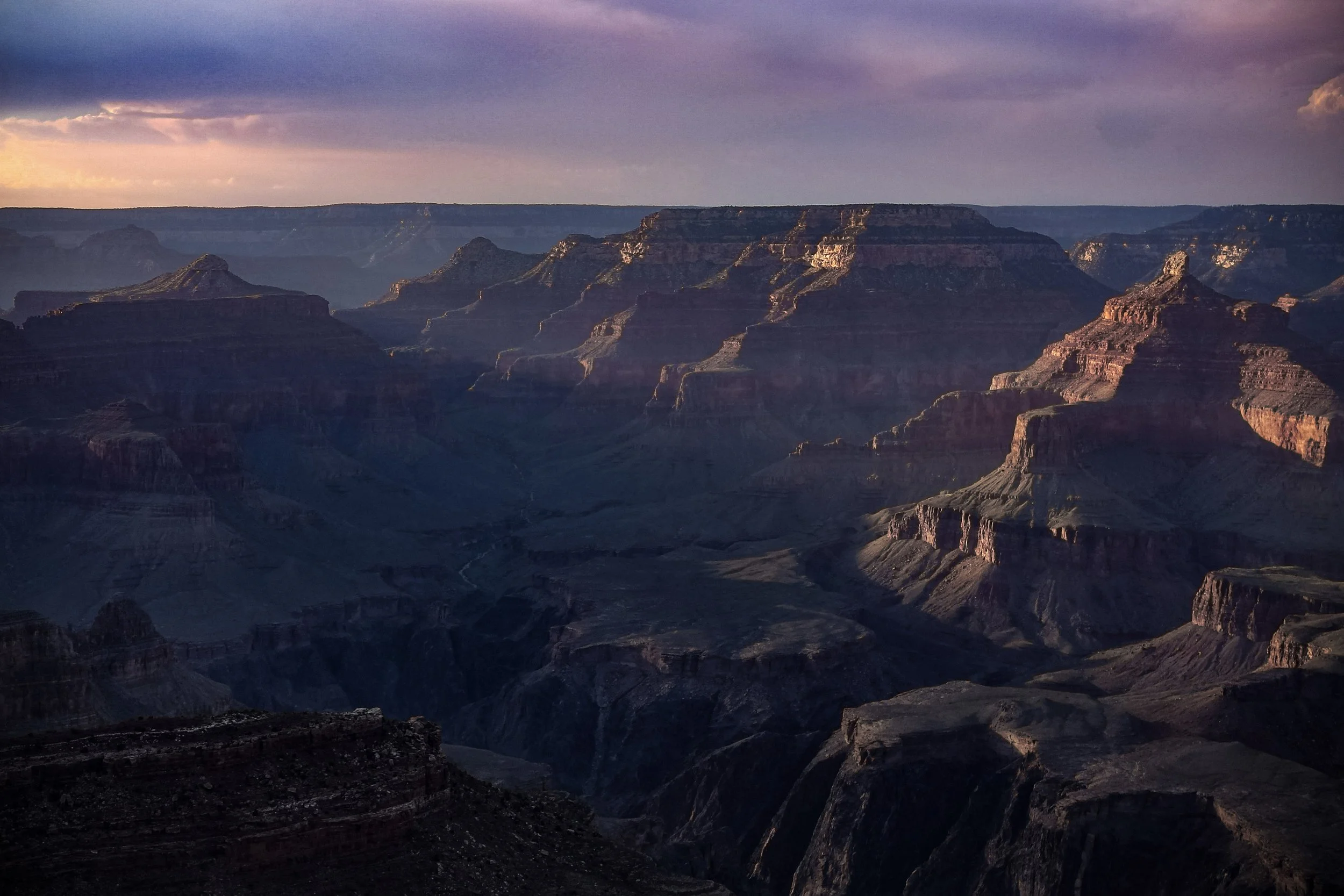 A landscape photograph of the Grand Canyon captured during a personal trip in 2015. The image focuses on the canyon’s layered depth, dramatic shadows, and warm light breaking across the rock formations, highlighting the scale and natural texture of t