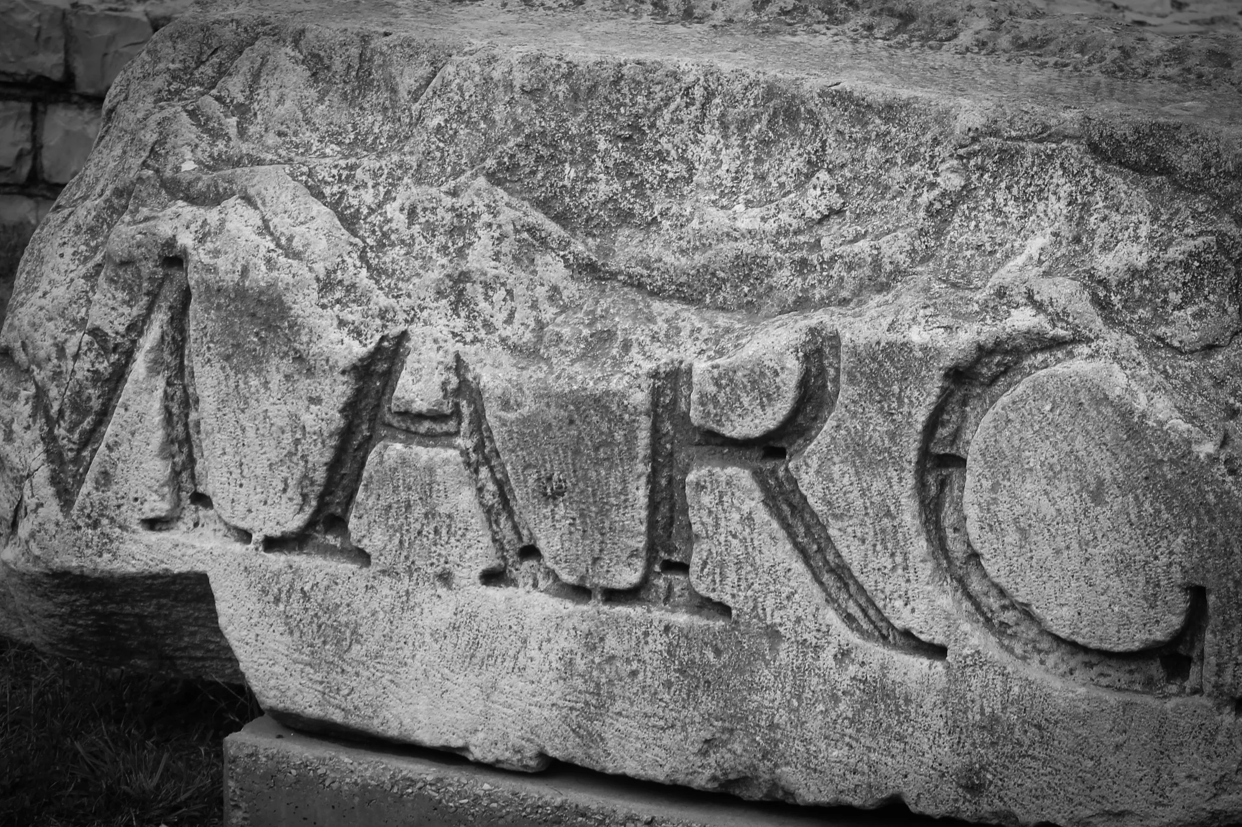 Close-up of an ancient stone carving with the inscription 'MARCO' on a weathered stone tablet.