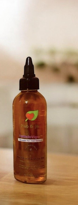 Amber glass dropper bottle with a black dropper cap, labeled 'Pao & Ju' and 'Rituals for real textures' on a wooden surface.