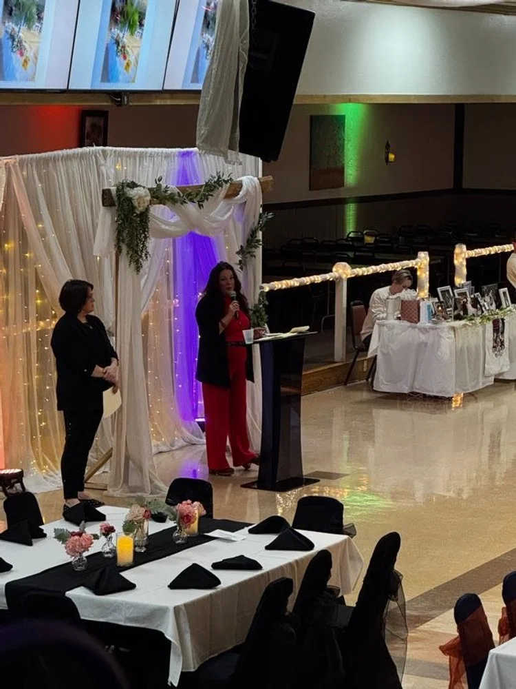 A woman speaking behind a podium at Center Stage, standing in front of a wedding arch and backdrop. 