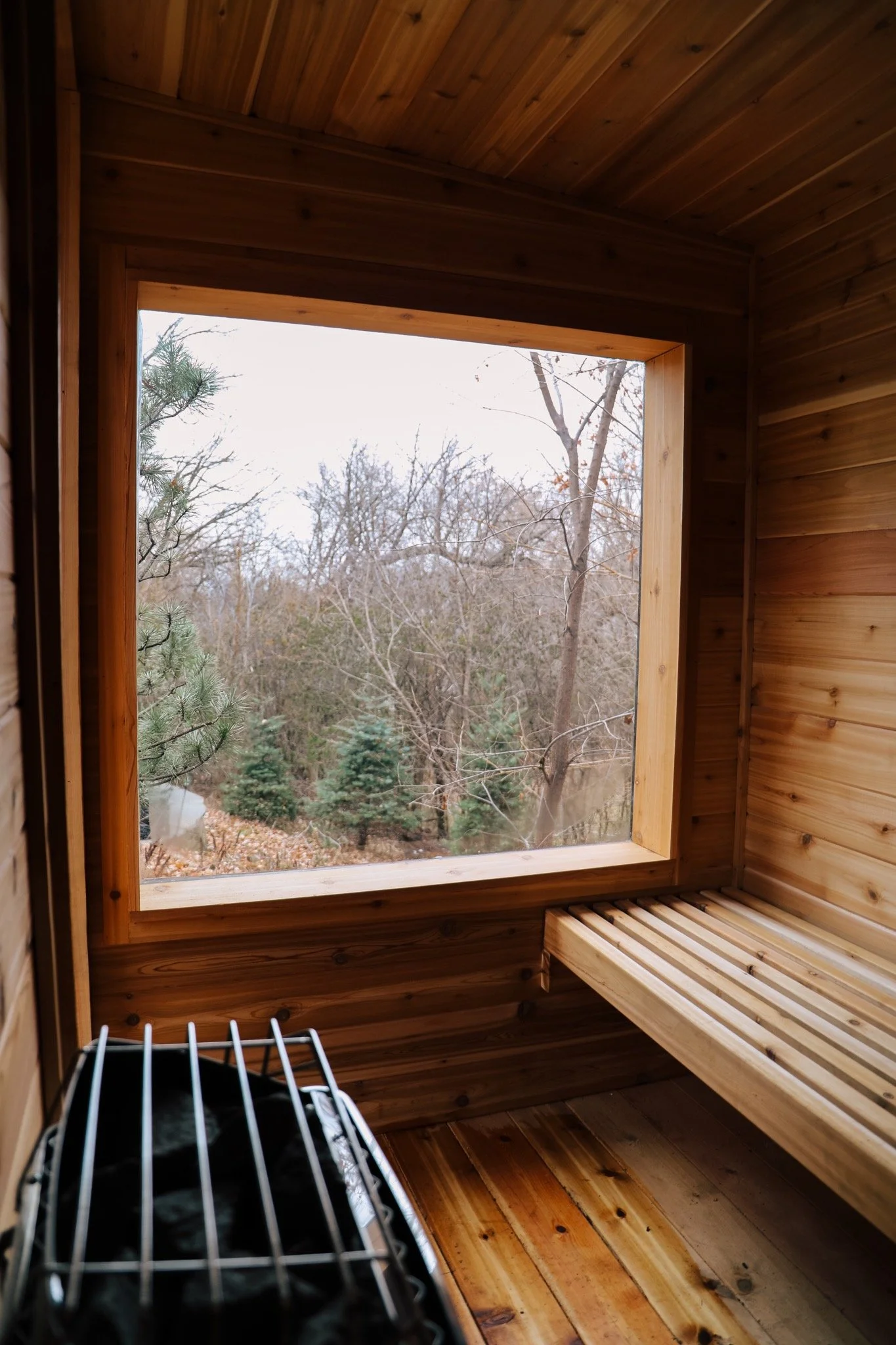 Interior of a small wooden sauna with a window overlooking trees and a pond.