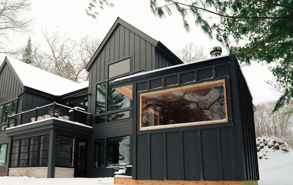 Modern black house with large windows and a snow-covered balcony in a winter landscape.
