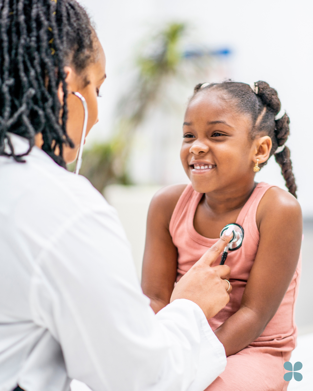 A young girl smiling as a doctor with a stethoscope examines her chest.