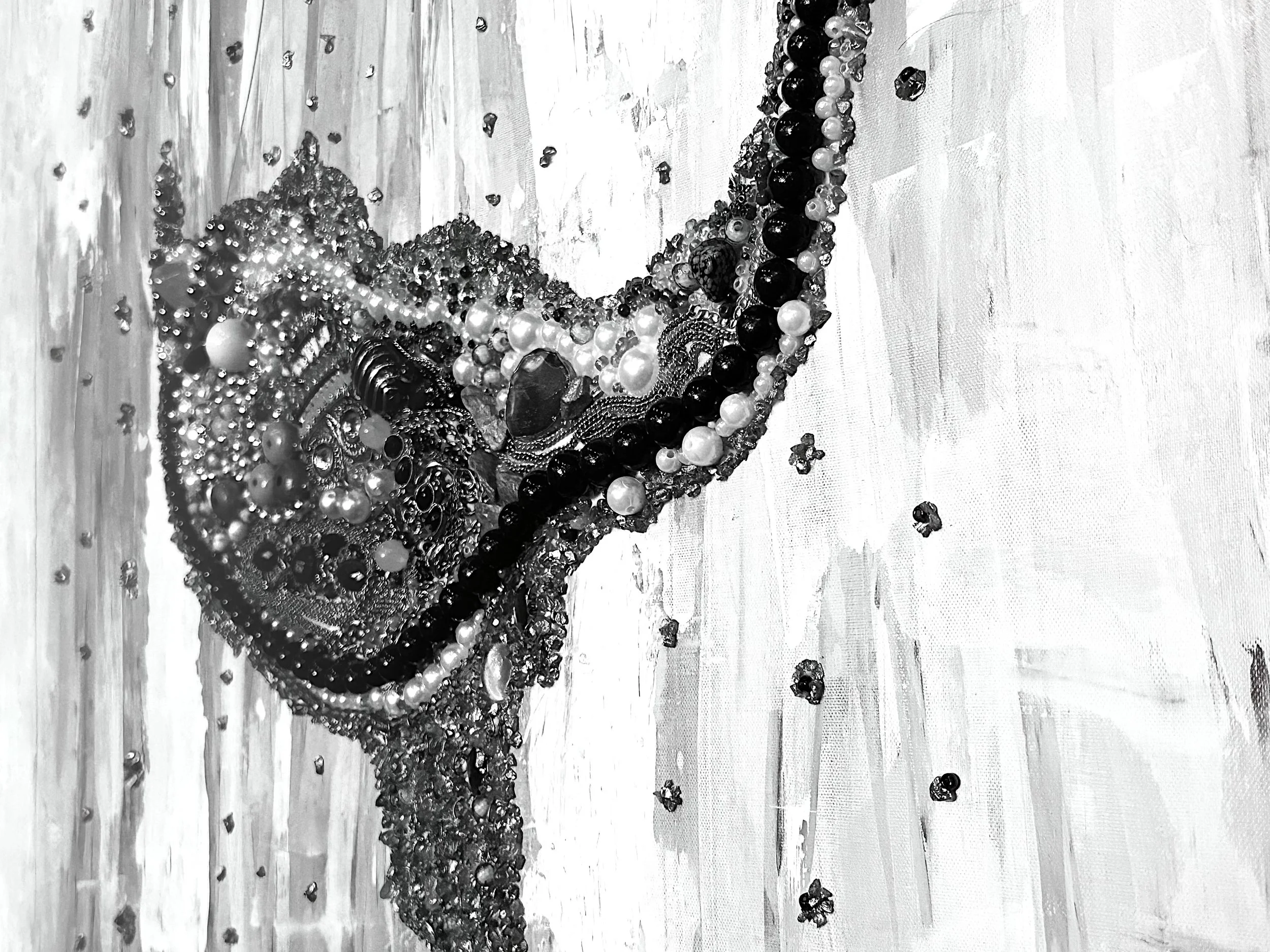 A black and white photo of a heart-shaped arrangement made from various sizes of pearls and dark beads, with some scattered around on a canvas.