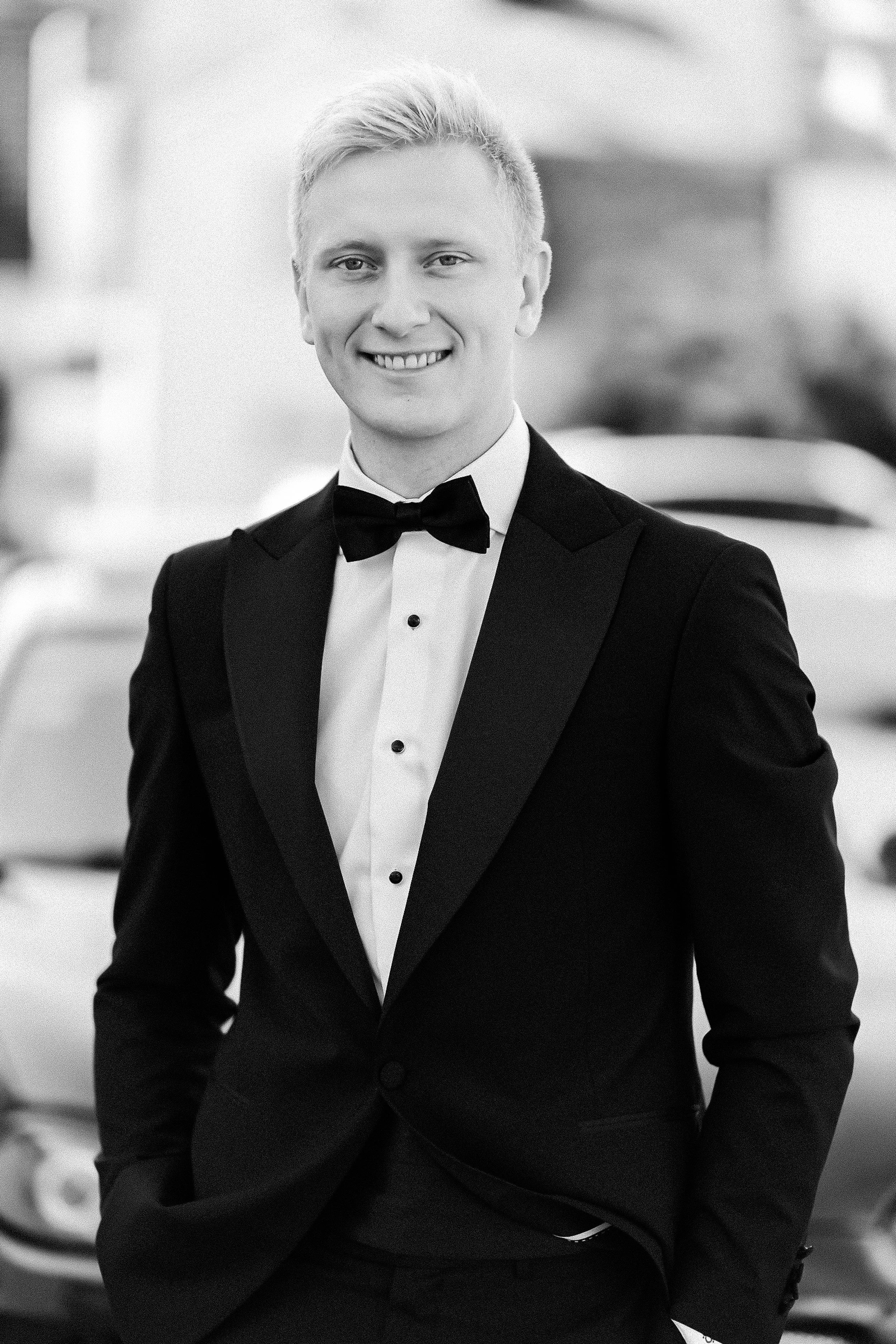 Smilende mann i svart smoking og sløyfe, fotografert i svart-hvitt.