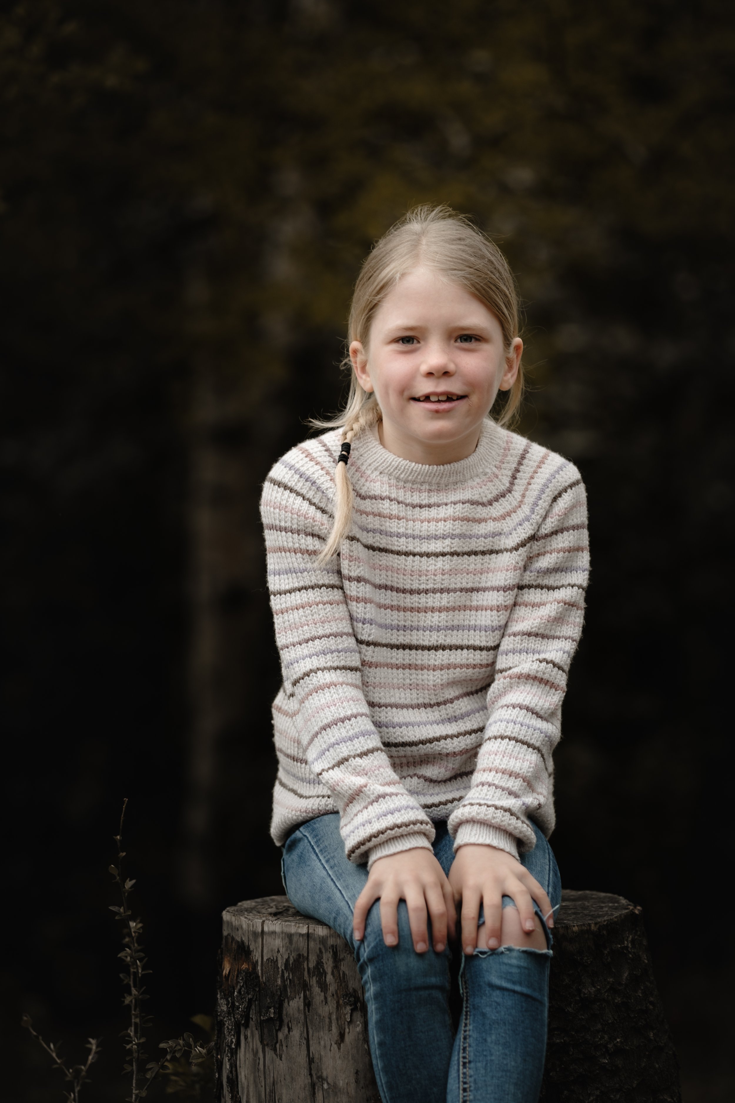 Smilende jente med fletter sitter på en trestubbe i skogen