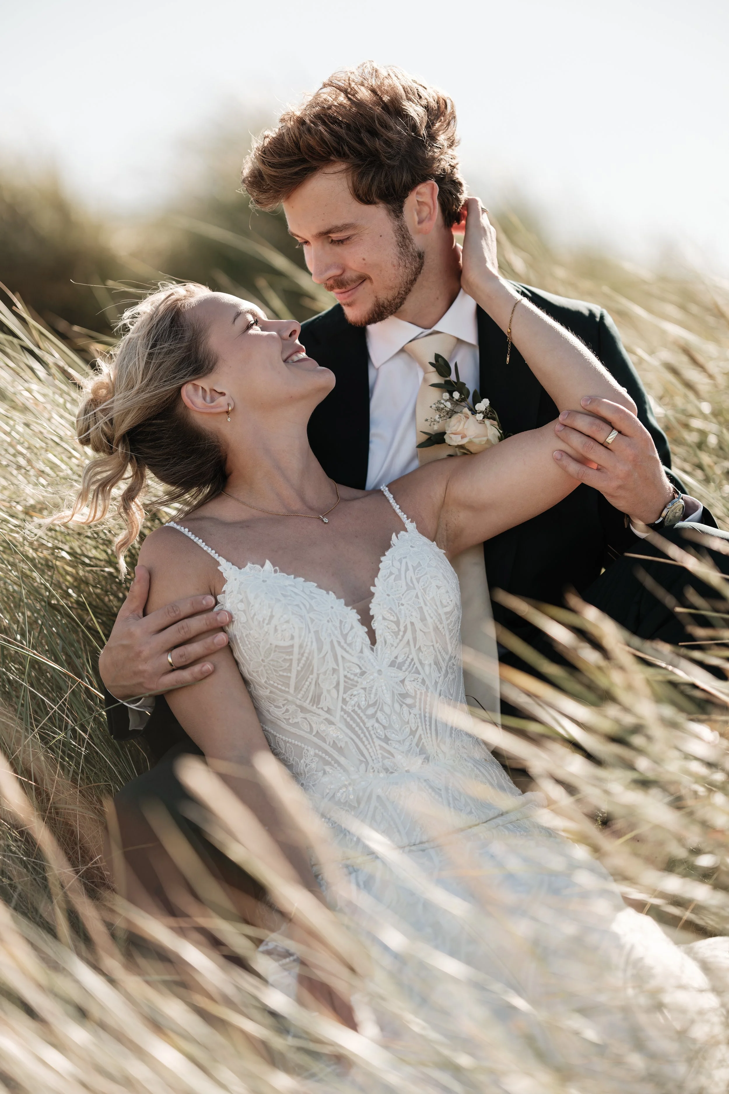 Et romantisk bryllupsbilde av et par som kysser og smiler mens de ligger i høstgras.