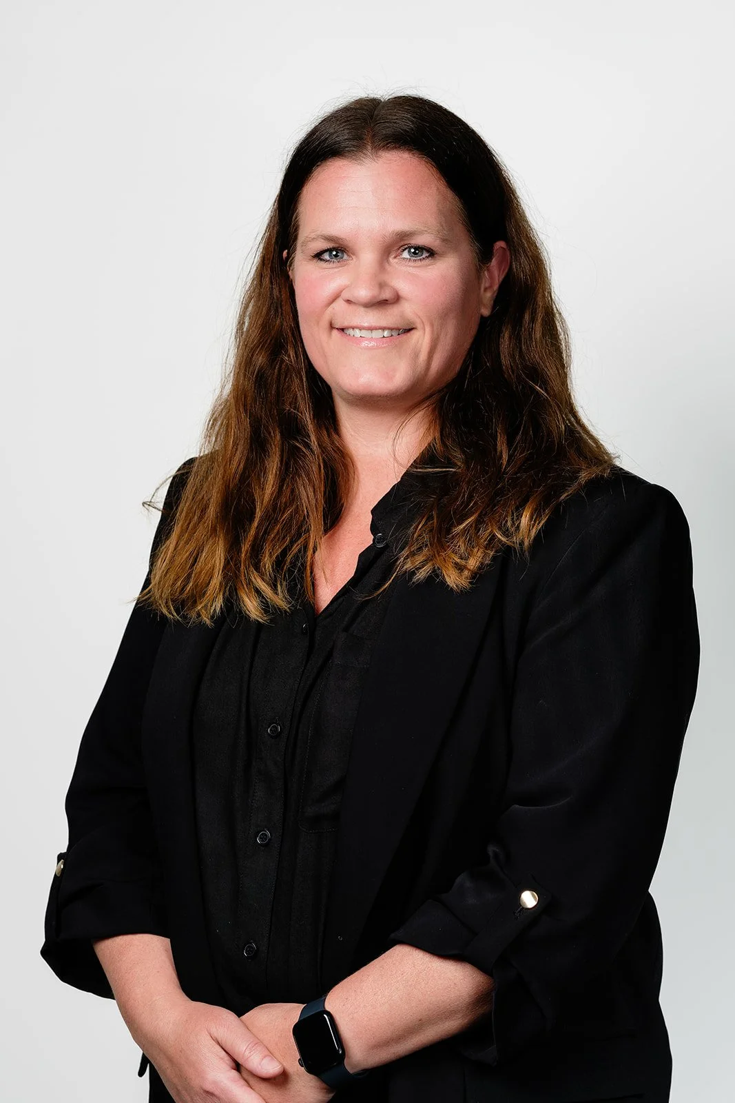 Portrett av en smilende kvinne med langt brunt hår i svart blazer og skjorte.