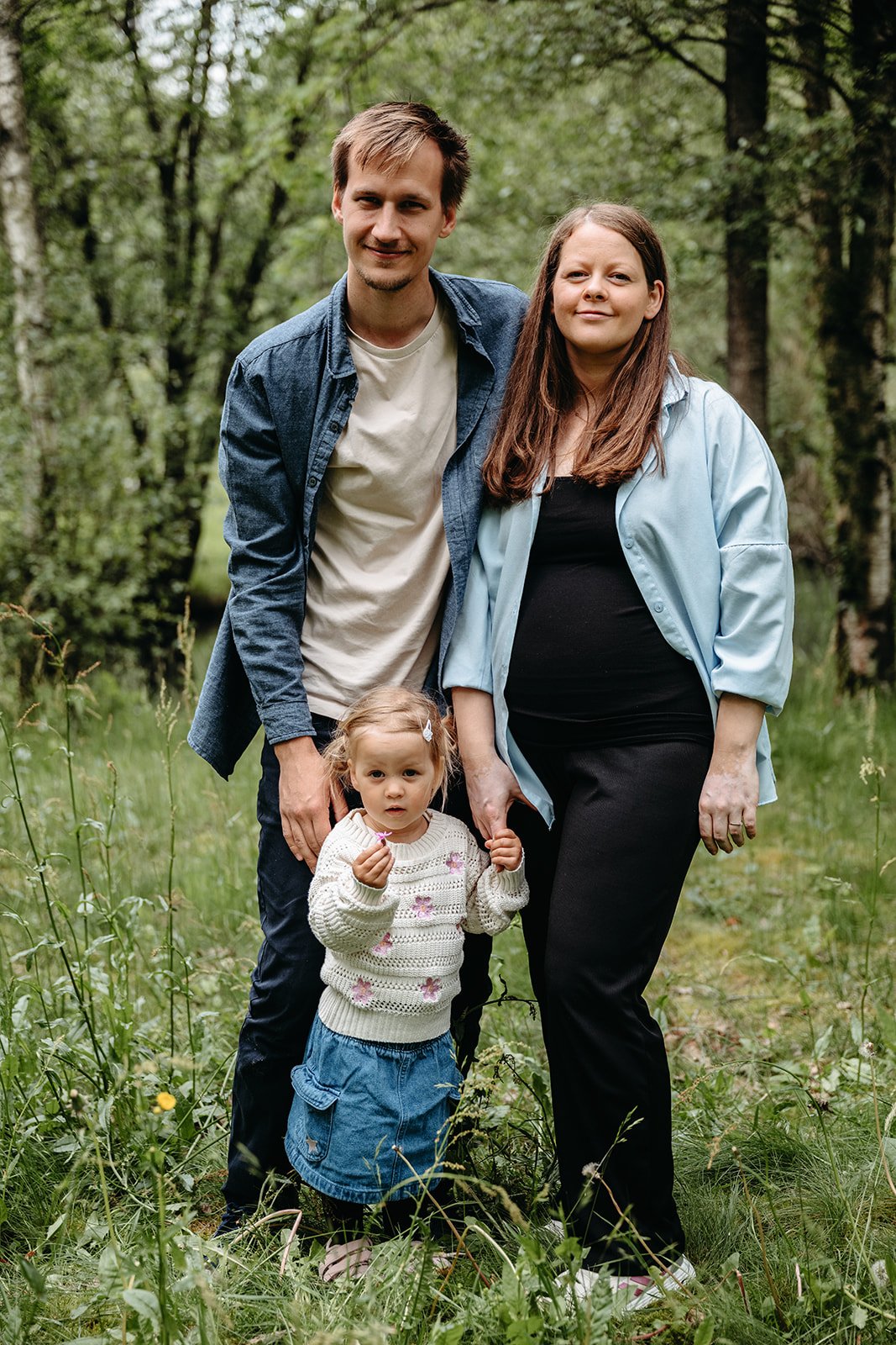 Familie på tre med gravid mor i en grønn skog