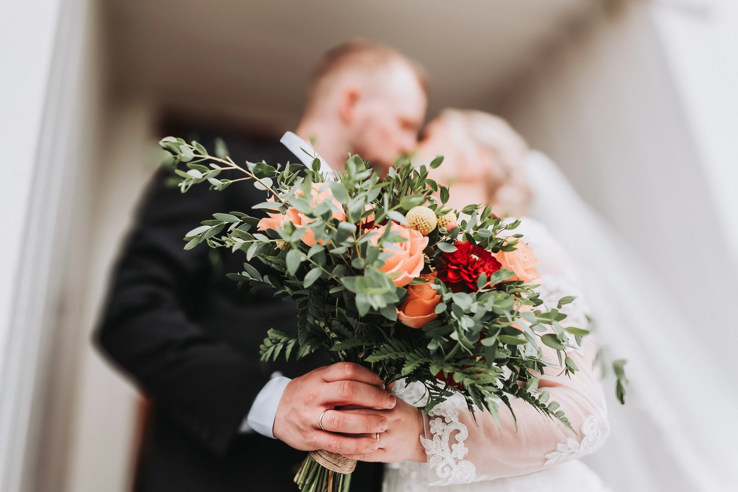 Et brudepar holder en stor blomsterbukett mens de står tett sammen, med fokus på buketten.