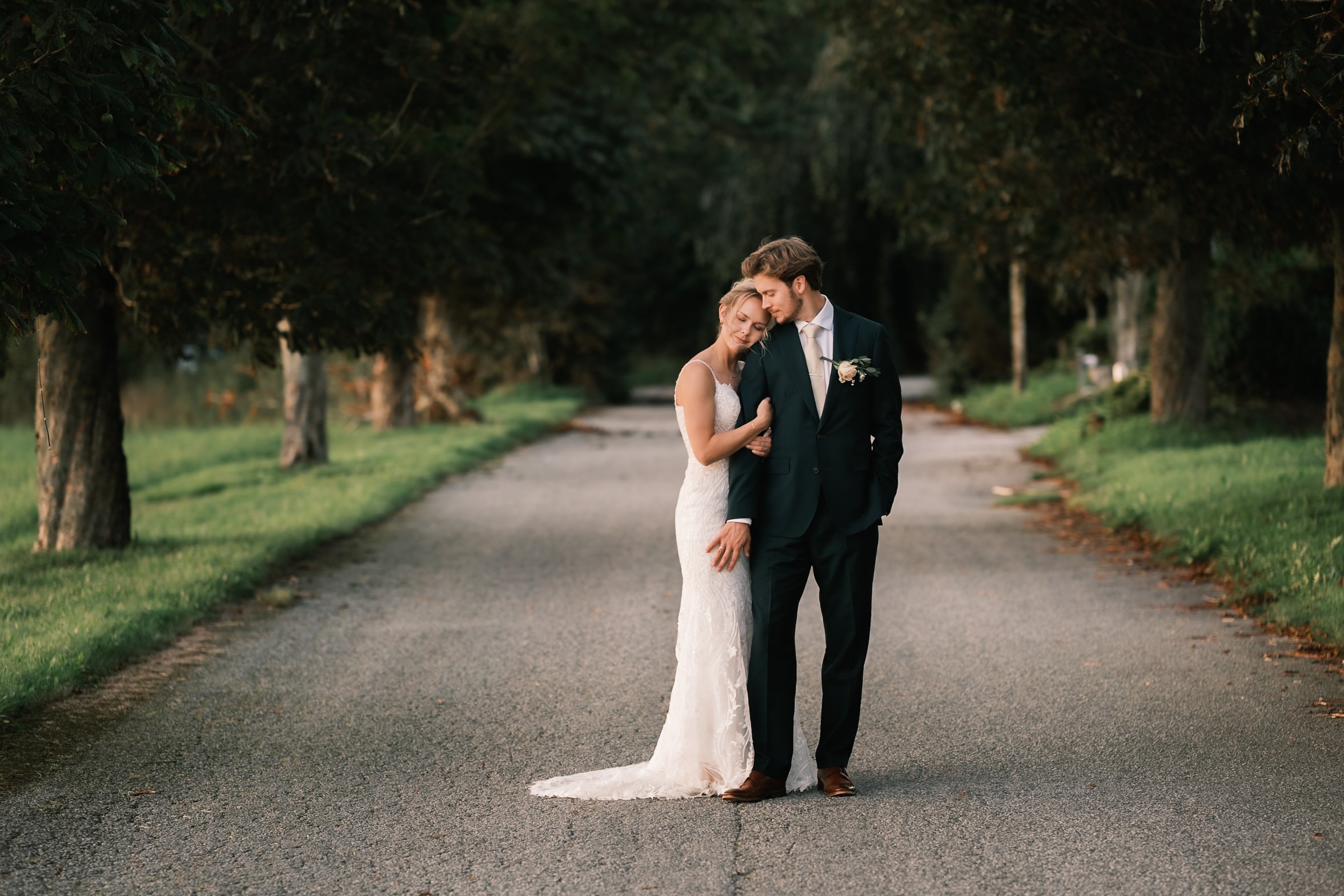 Et brudepar går på en tre-lane vei omgitt av grønne trær, med solnedgangsbelysning.