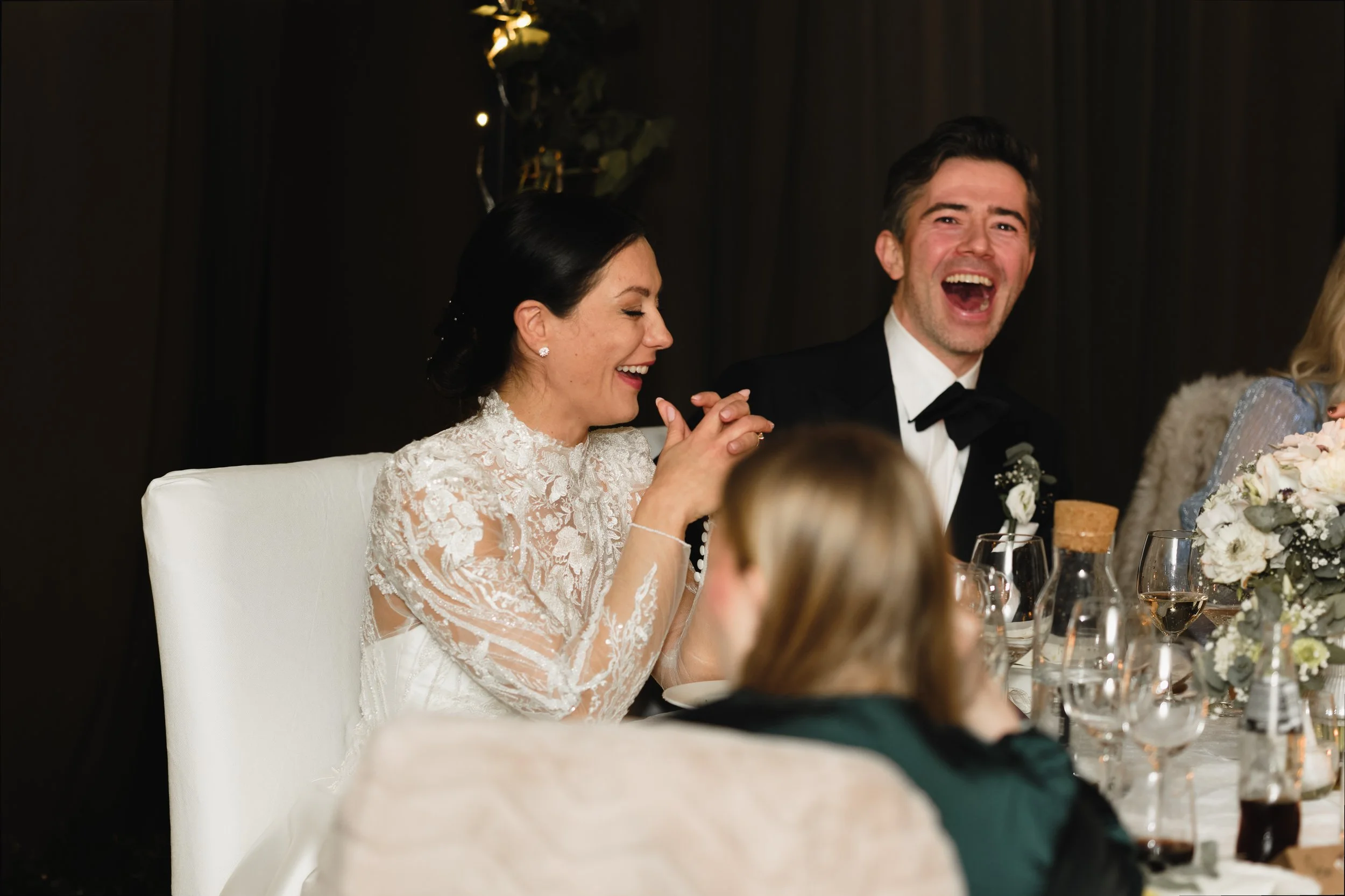 Et lykkelig bryllupsselskap med en mann i smoking og en kvinne i en hvit brudekjole, som ler og har det moro under bryllupsfeiring.