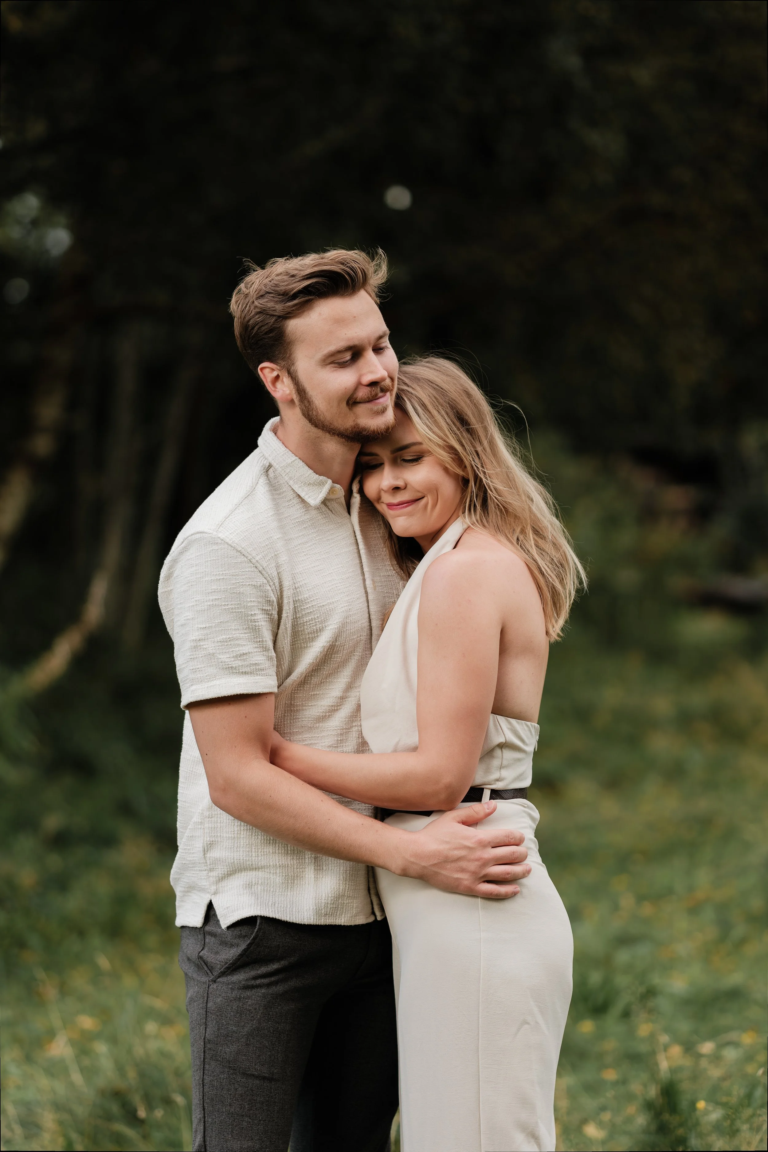 To personer omfavner og smiler i en grønn utendørs setting.