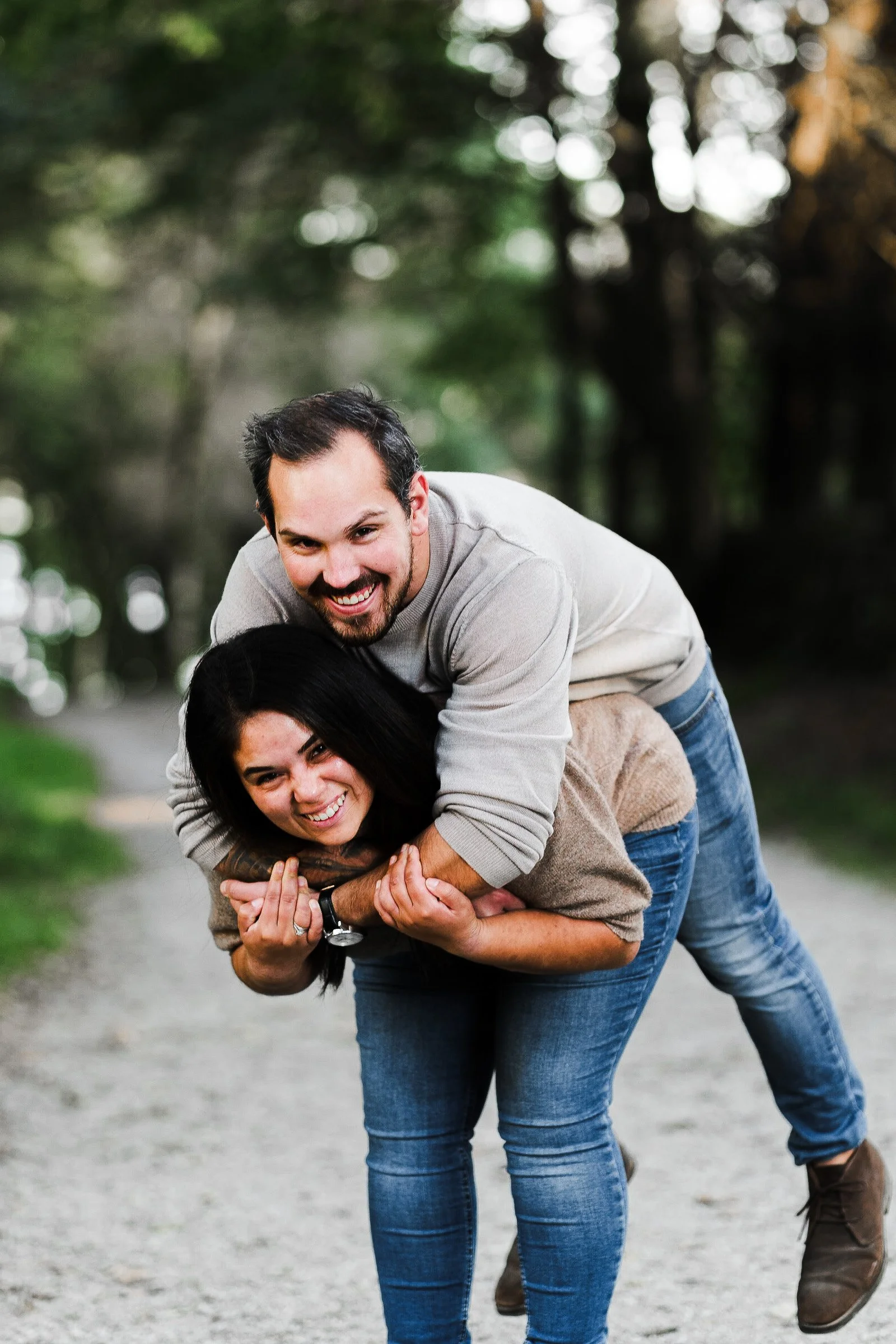 To personer på en skogssti, en mann som ler og henger over en kvinne som smiler, de leker og har det gøy ute i naturen.