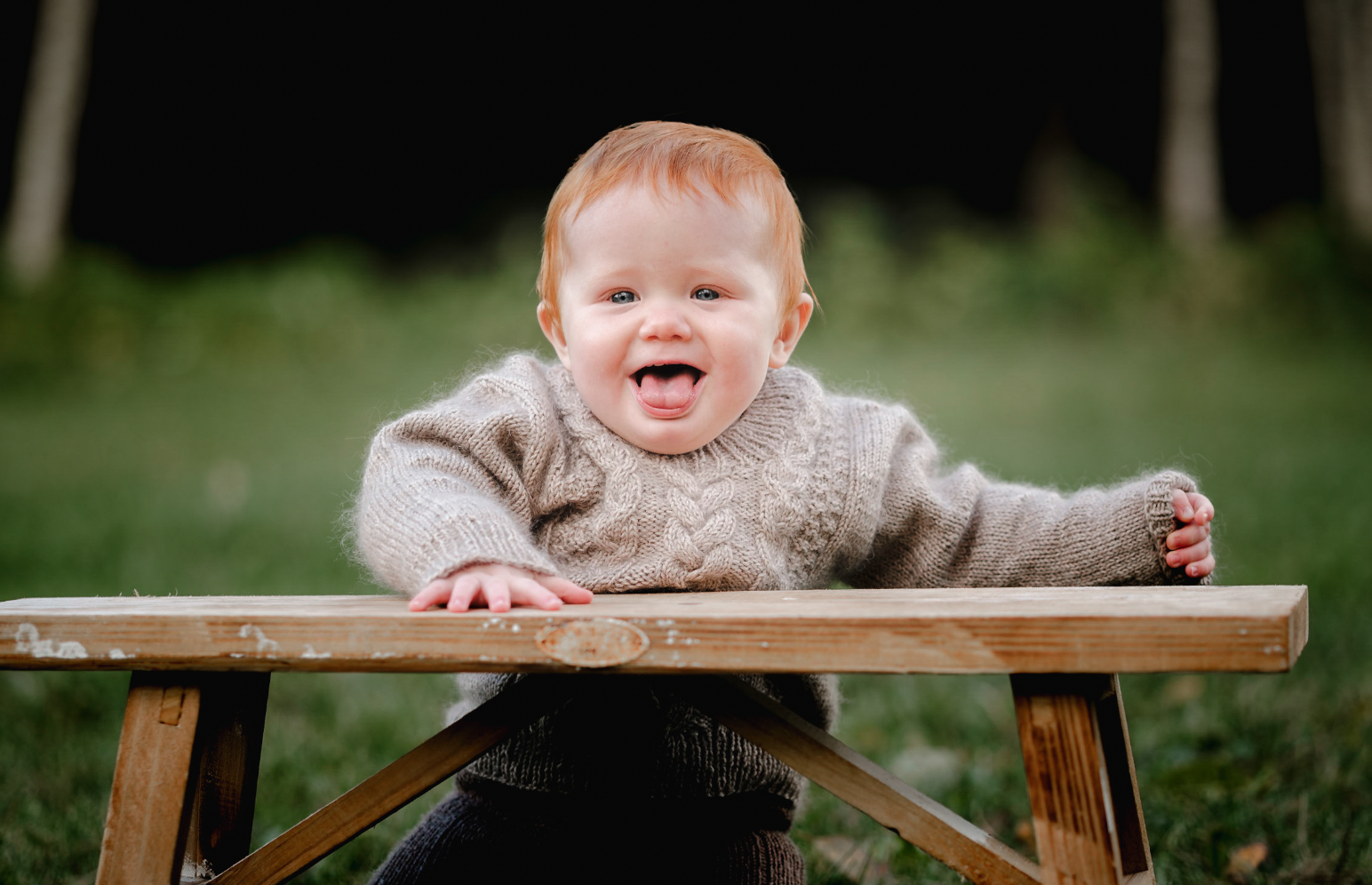 Ung gutt med rødt hår som smiler og leker ute på gresset med et trebord.