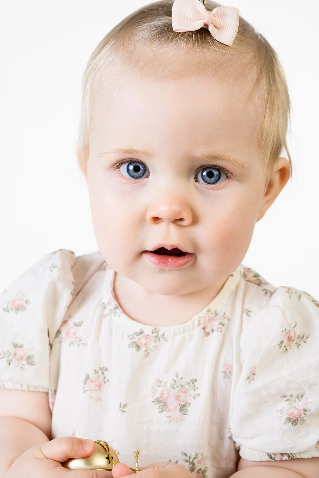 Nærbilde av en blond babyjente med blå øyne, rosa sløyfe og blomstrete kjole