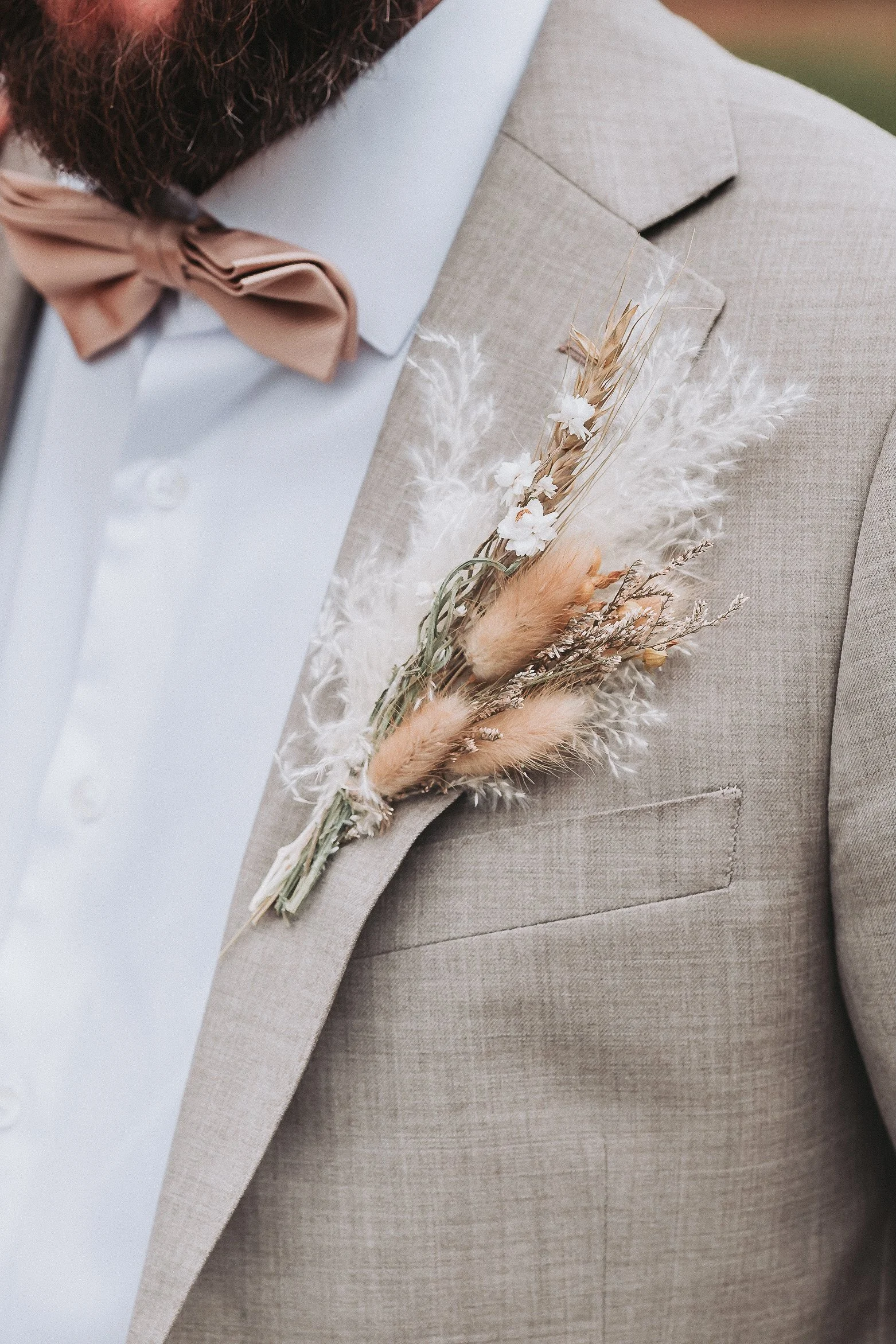 Nærbilde av en brudgom i lys beige lindress med tørket blomsterboutonnière og beige sløyfe.