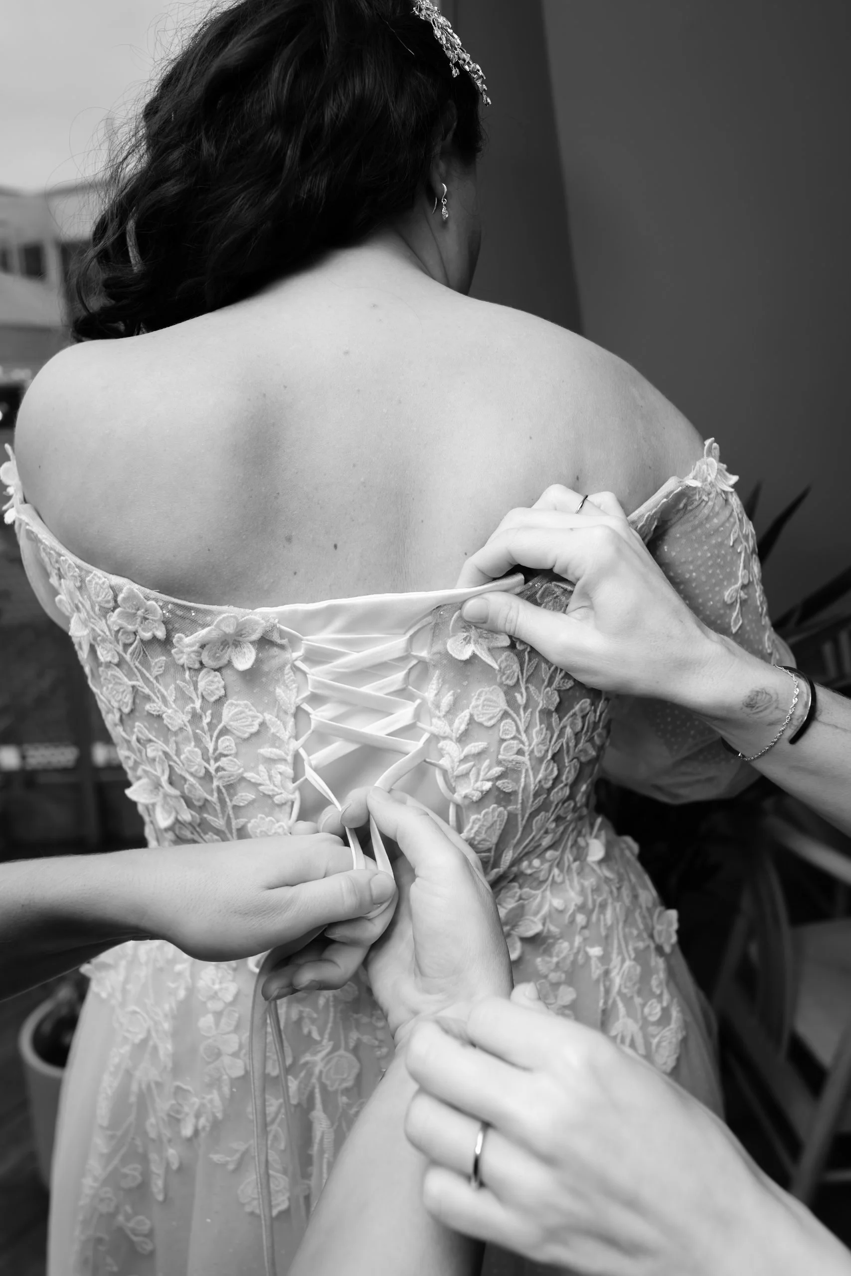 En kvinne i en brudekjole får hjelp til å knyte opp snøring på ryggen av kjolen.