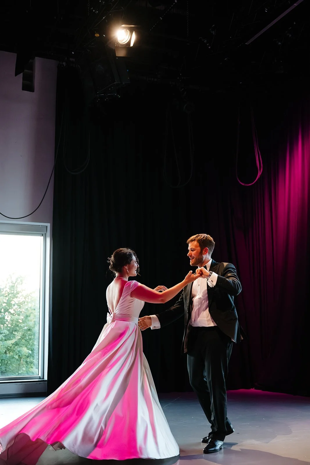 Par danser vals på en scene, med kvinnen i rosa kjole og mannen i svart smoking under scenelys.
