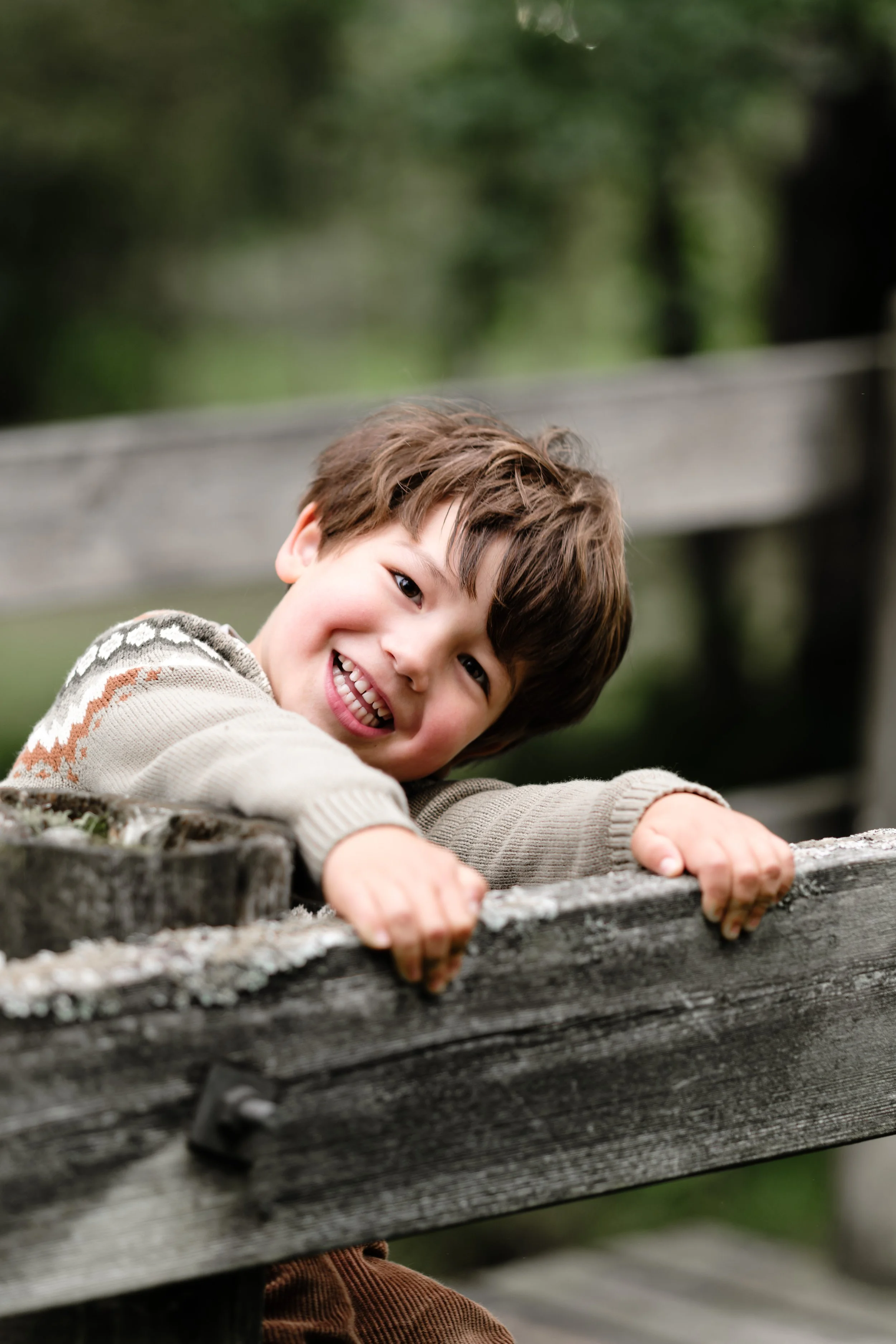 Liten gutt smiler og leker på en trebenk utendørs.