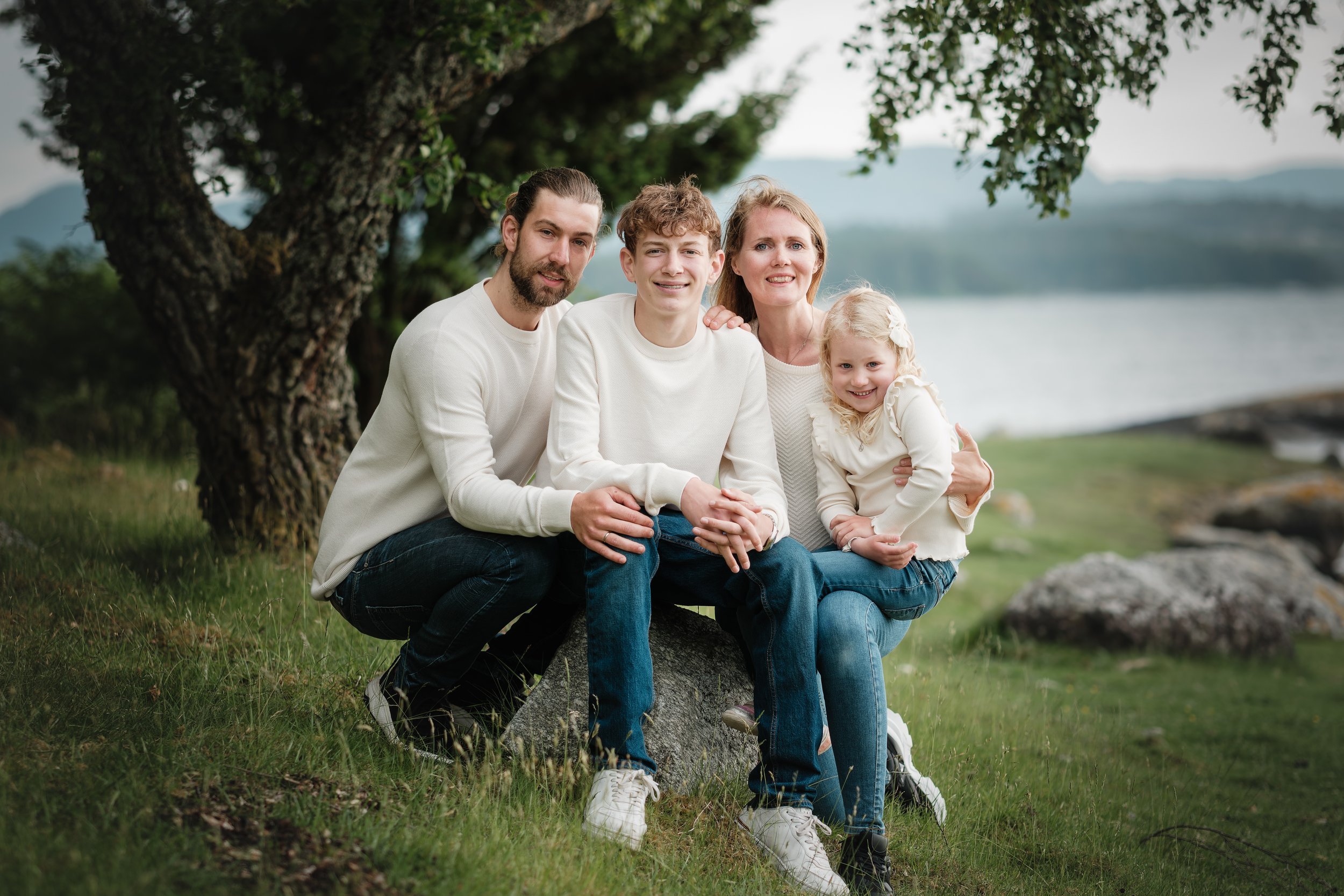 Familie på fire poserer ved et tre med utsikt over en innsjø og fjell