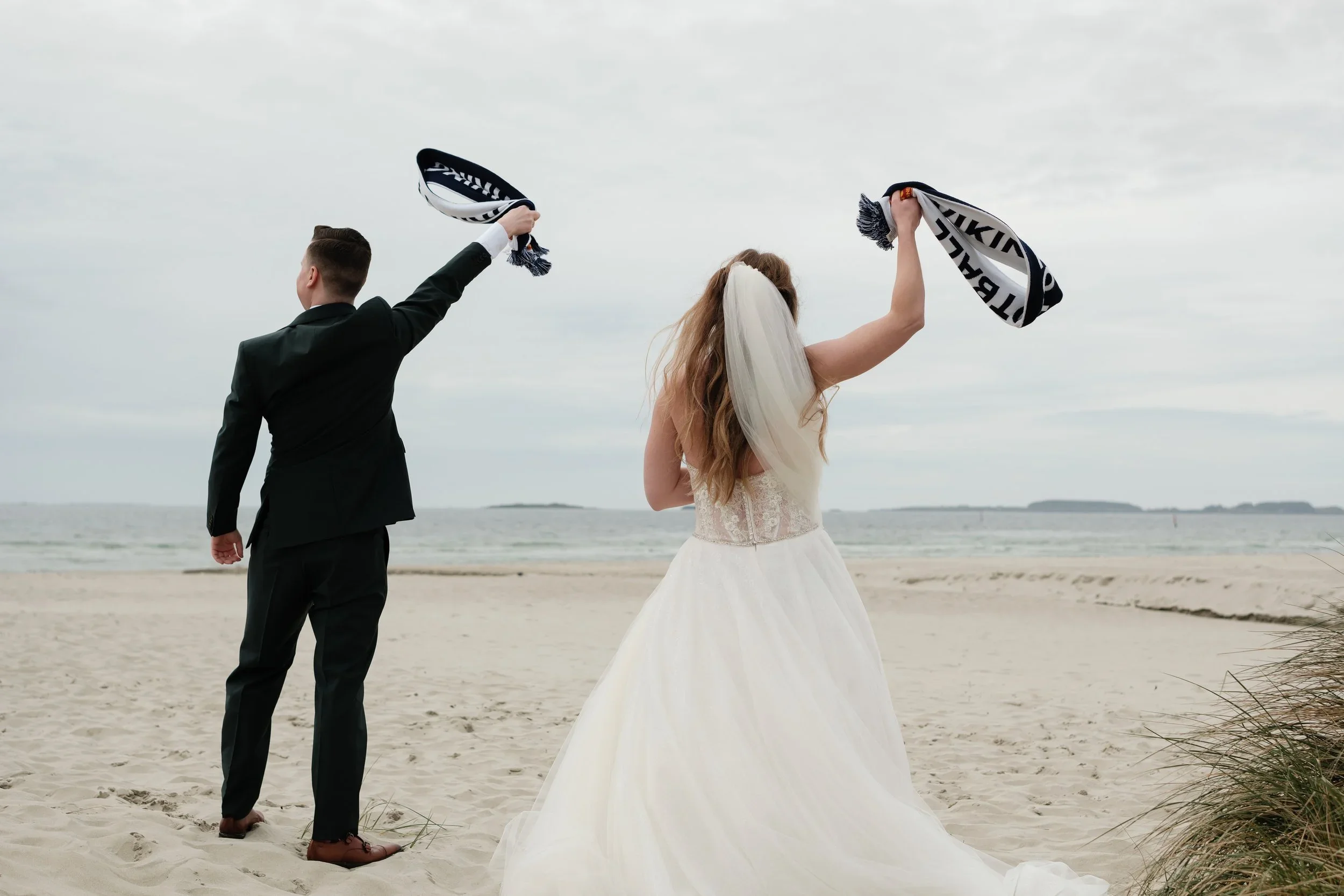 Brudepar på stranden med skjerf hevet over hodet ved havet