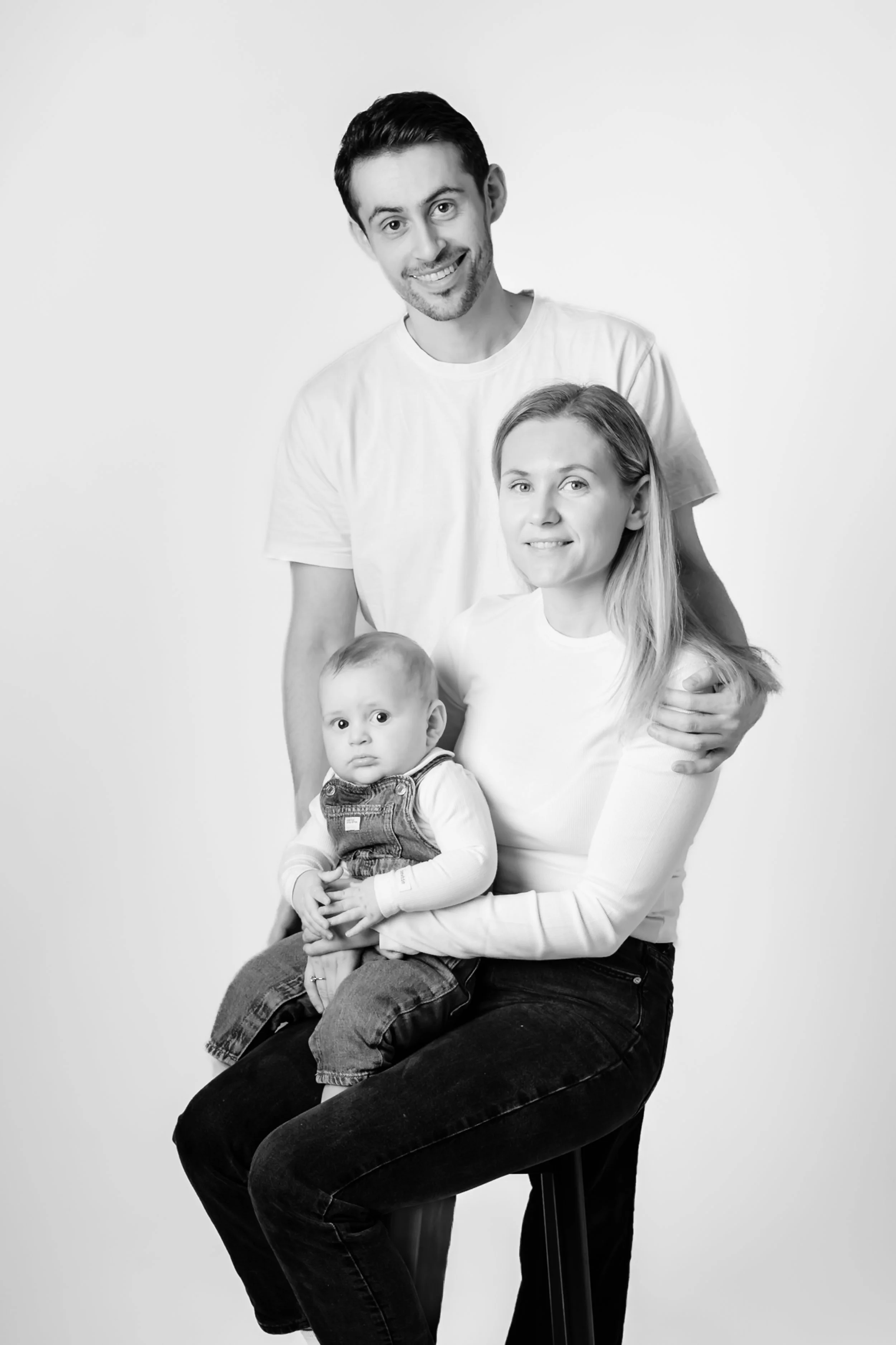 Svart-hvitt familiebilde av en smilende far, mor og baby.