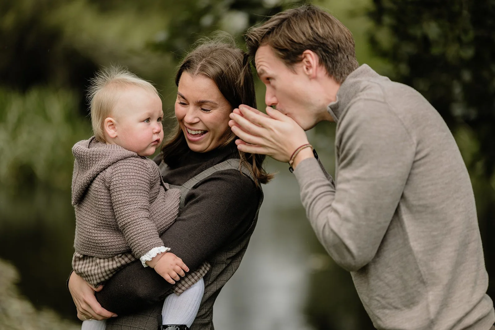 Familie med baby ler sammen utendørs i en grønn park