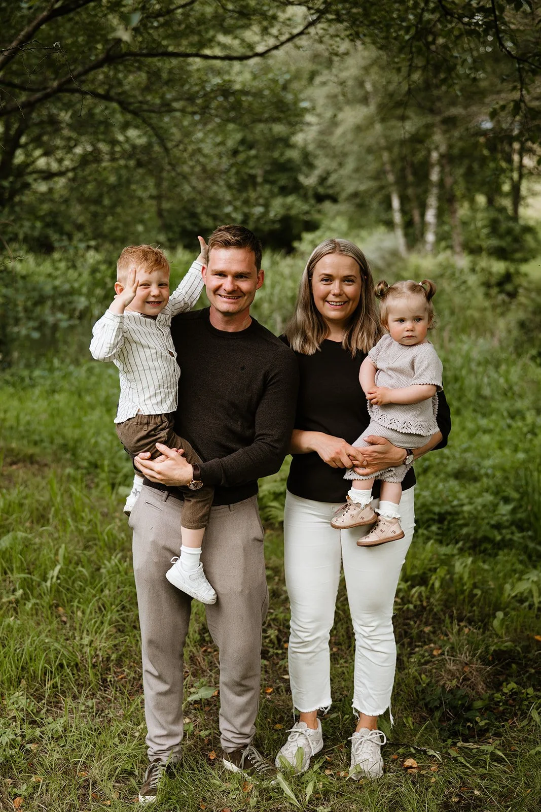 Familie på fire poserer i en frodig skog; foreldrene holder hvert sitt barn.
