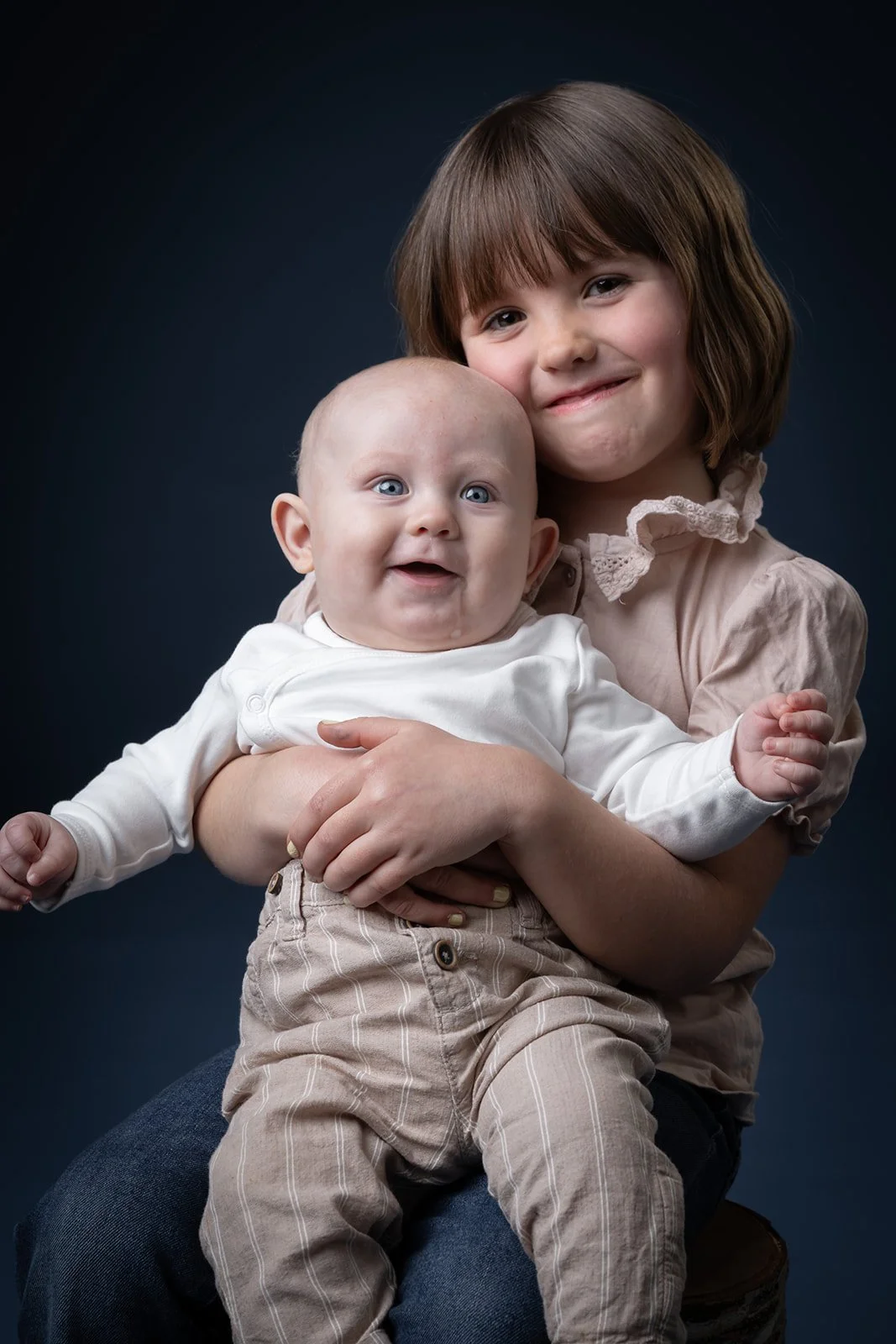 Smilende jente holder en baby i fanget foran mørk bakgrunn.