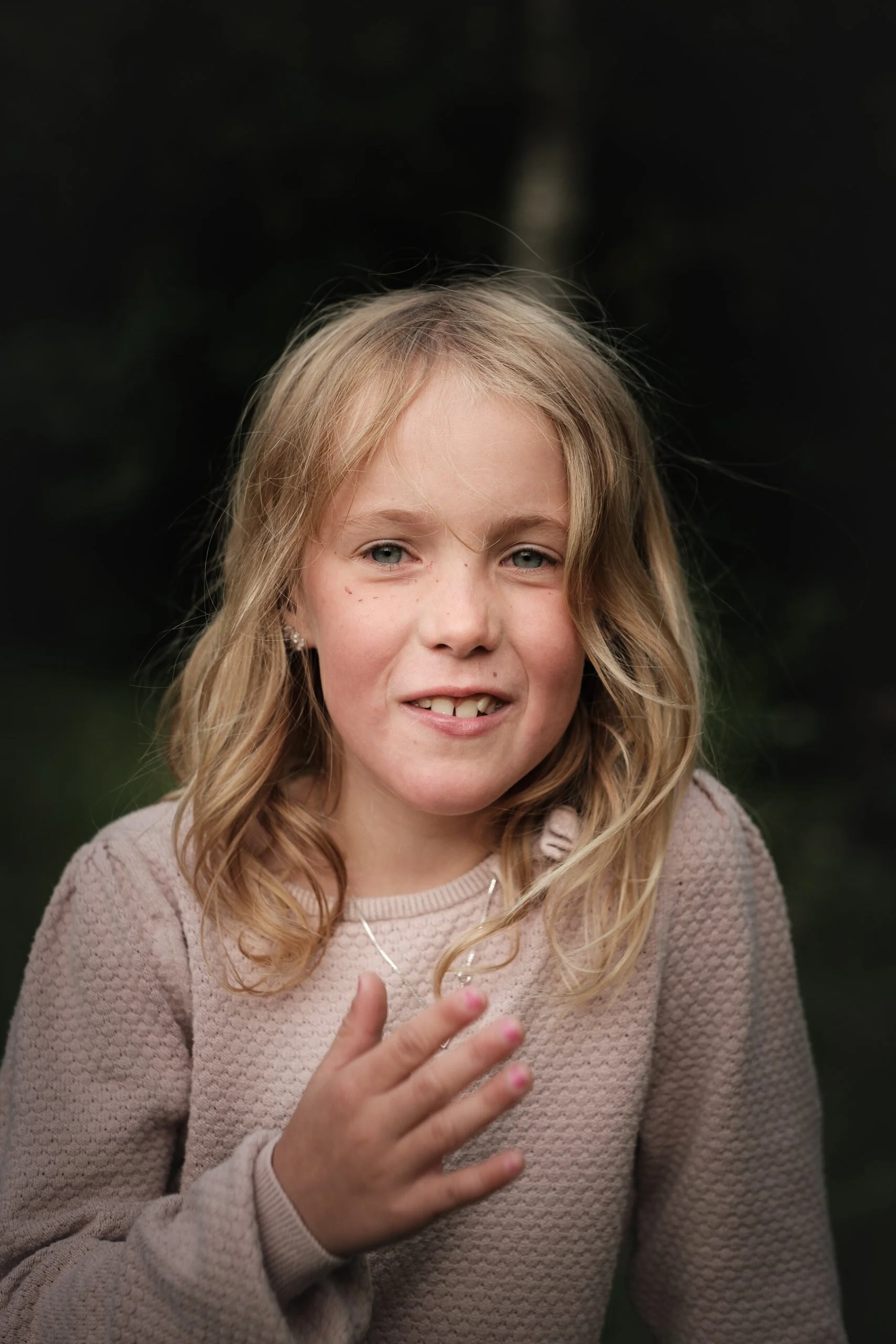 Smilende blond jente i rosa genser med hånden på brystet