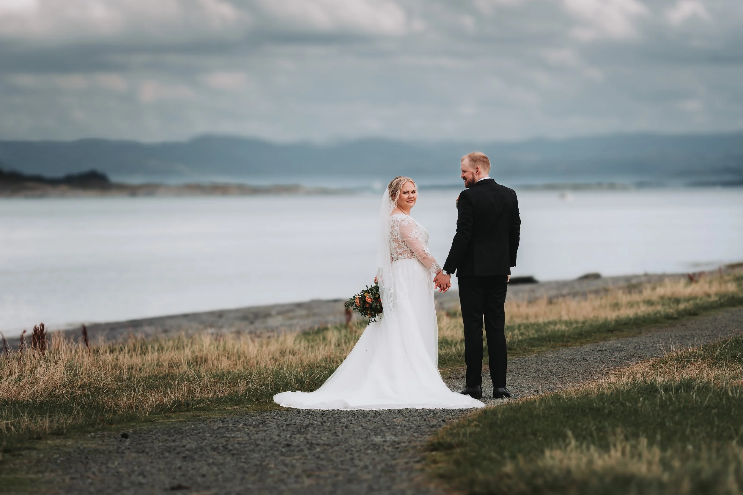 En brud og en brudgom holder hender ved sjøen under en bryllupsseremoni.