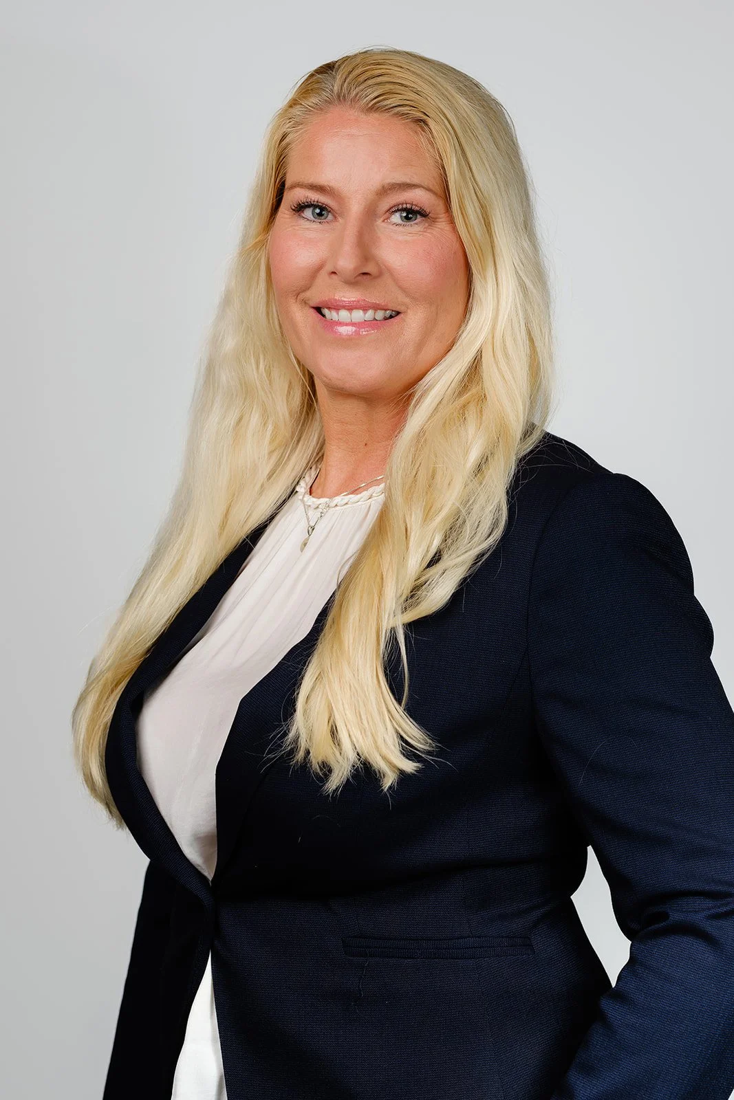Profesjonelt portrett av en smilende blond kvinne i mørk blazer mot lys bakgrunn
