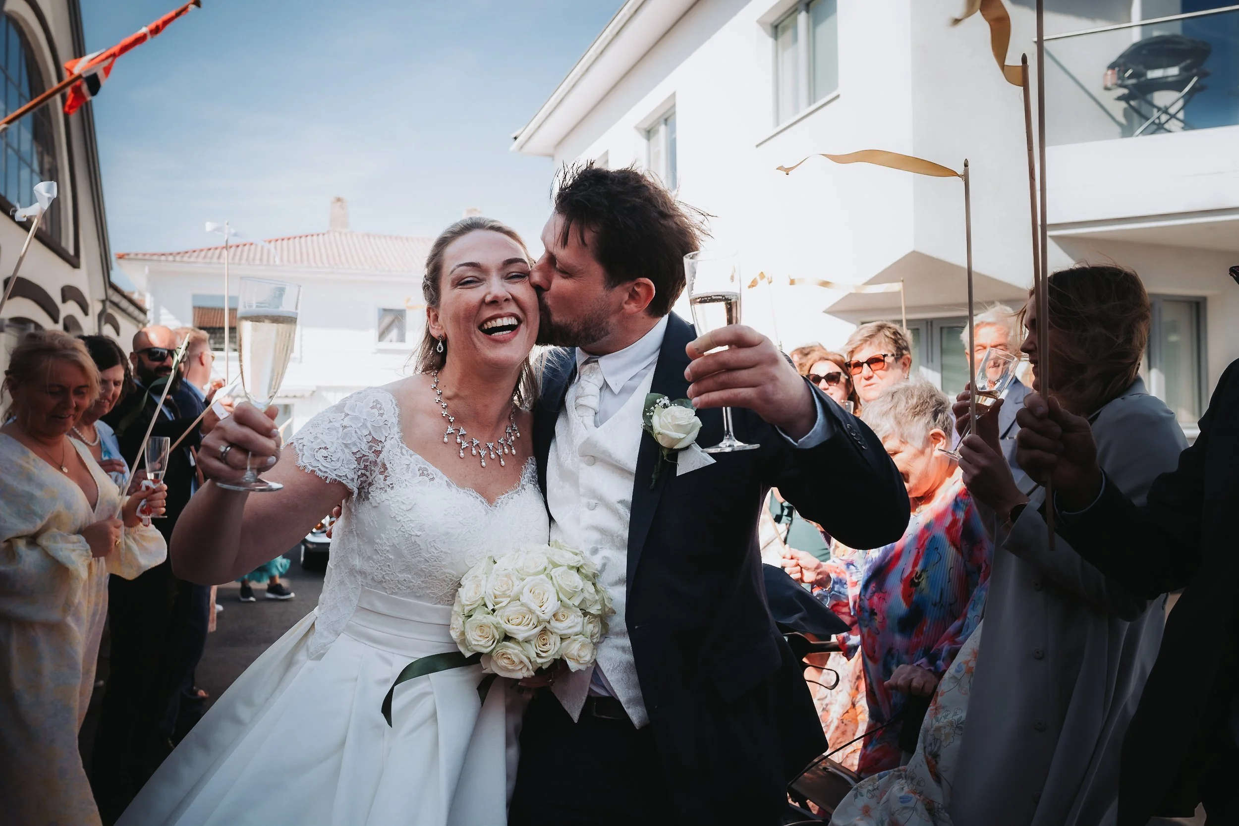 Brudepar kysser og skåler med champagne mens bryllupsgjester jubler rundt dem
